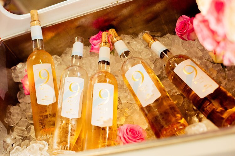 Six bottles of pink rosé wine in ice-filled cooler with pink roses around.