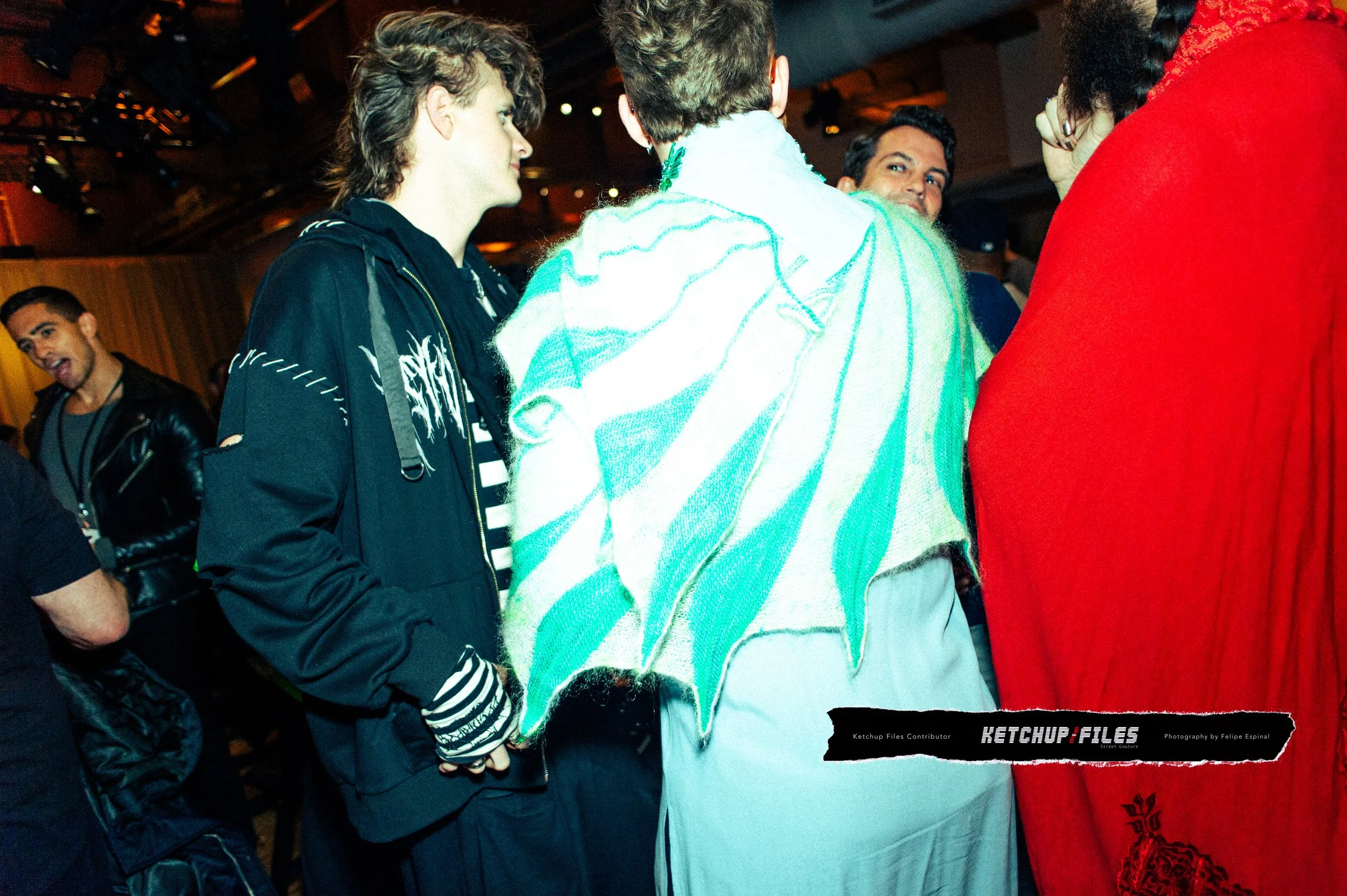 Group of young people socializing at a party, some wearing casual and stylish clothing, in a lively indoor setting with warm lighting.