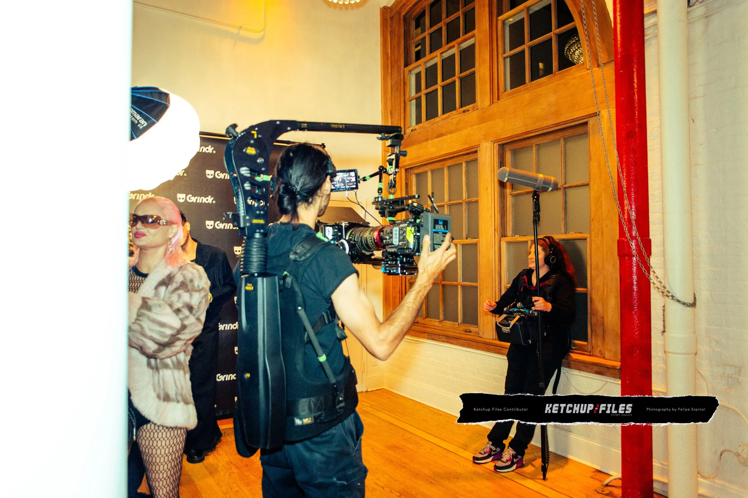 Camera crew filming a woman with headphones in front of a wooden window during a media event