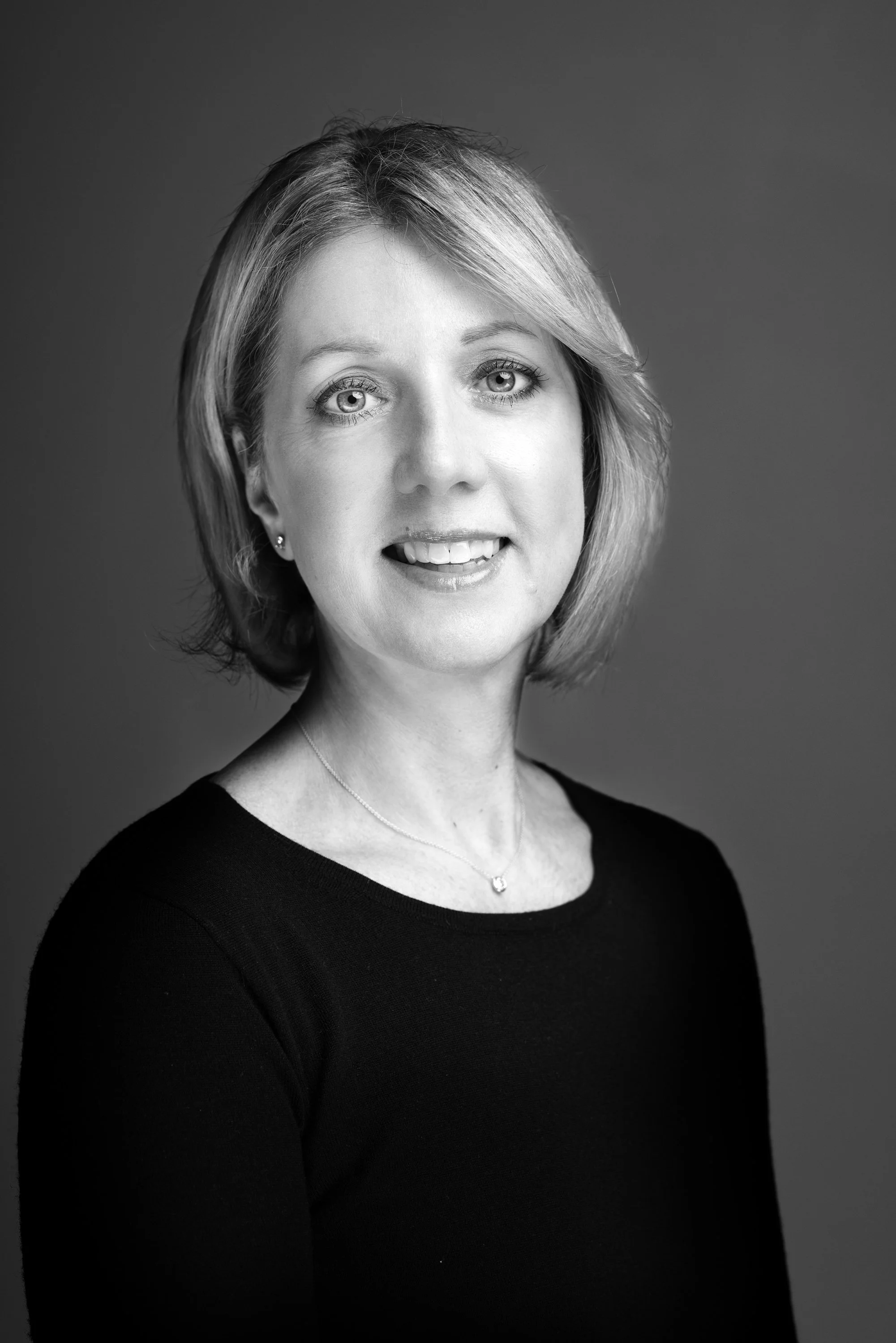 Black and white portrait of a woman with short hair, wearing a black top and a necklace, against a plain background.