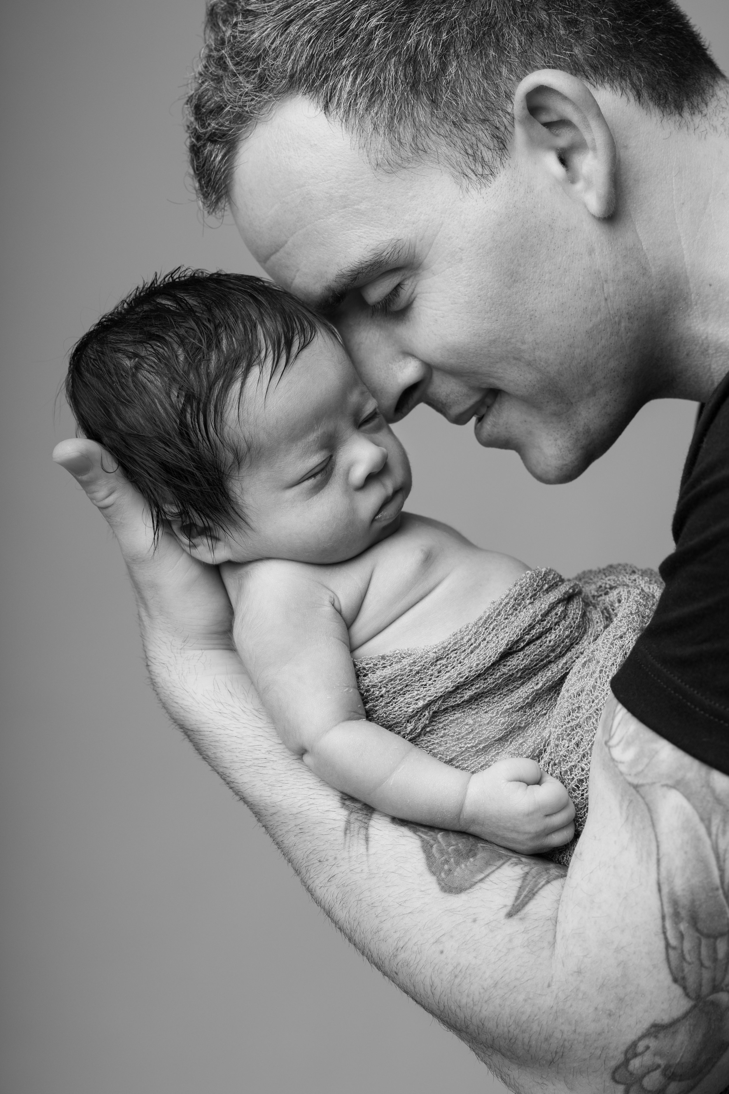 A black and white photo of a man with short hair holding a sleeping child with wet hair close to his face, both with peaceful expressions.