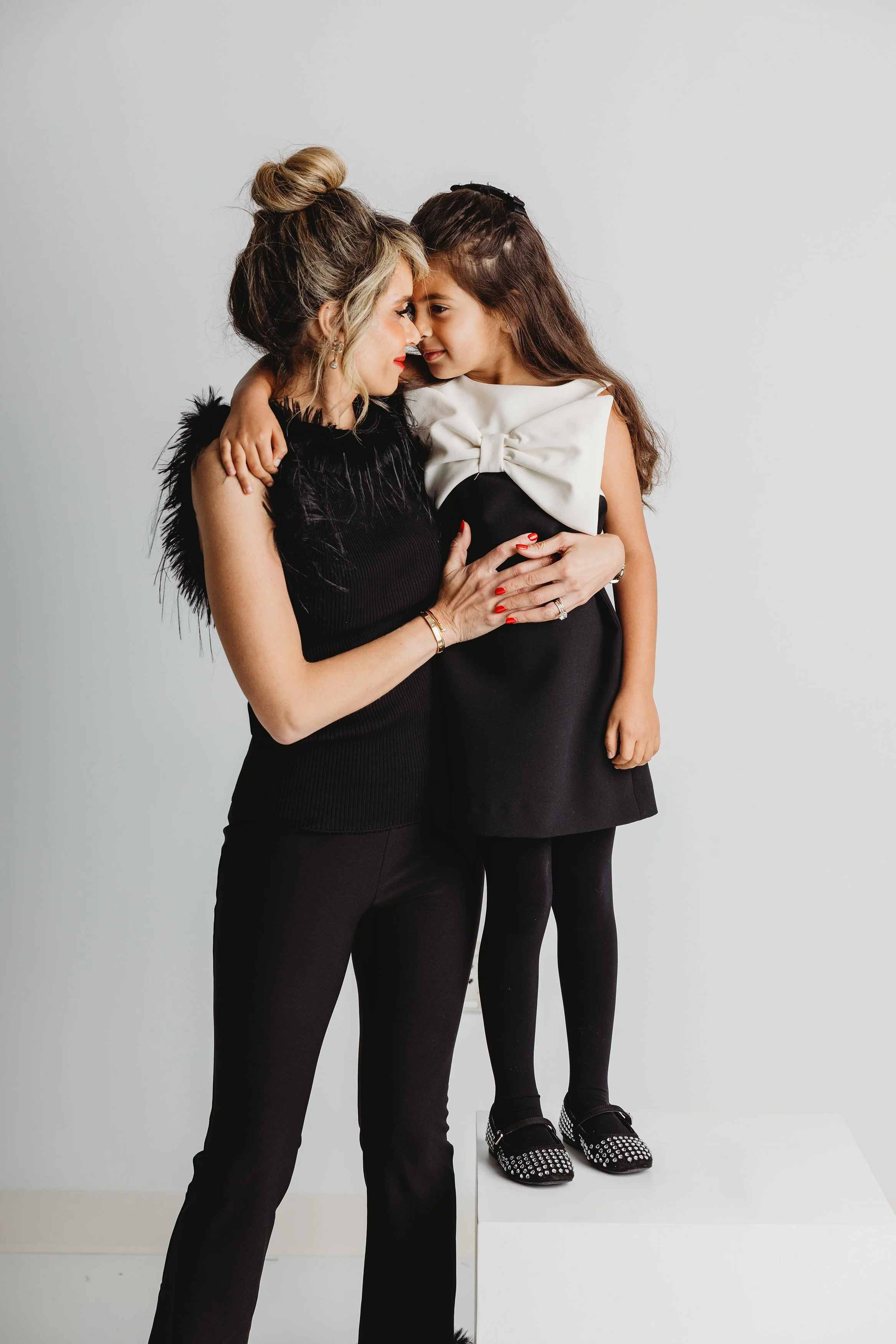 Mother and daughter sharing a tender moment, face to face, with foreheads touching against a plain white background.