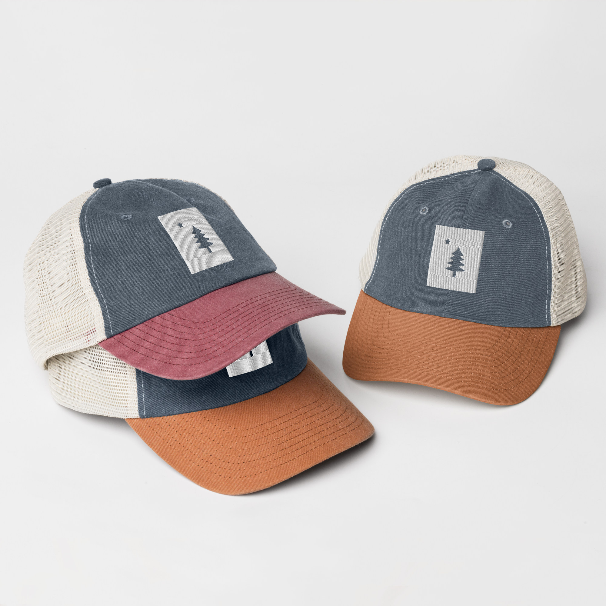 Two caps with color-blocked designs, featuring mesh back panels and a patch with a tree and star symbol on the front, in neutral and earthy tones.