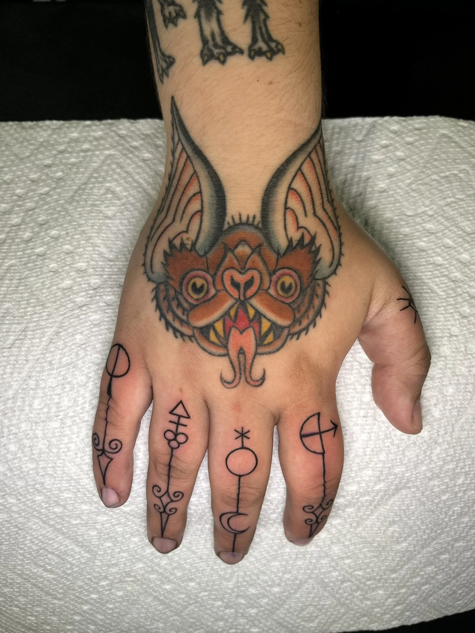 Traditional style bat tattoo on a hand with alchemical style symbols on the fingers