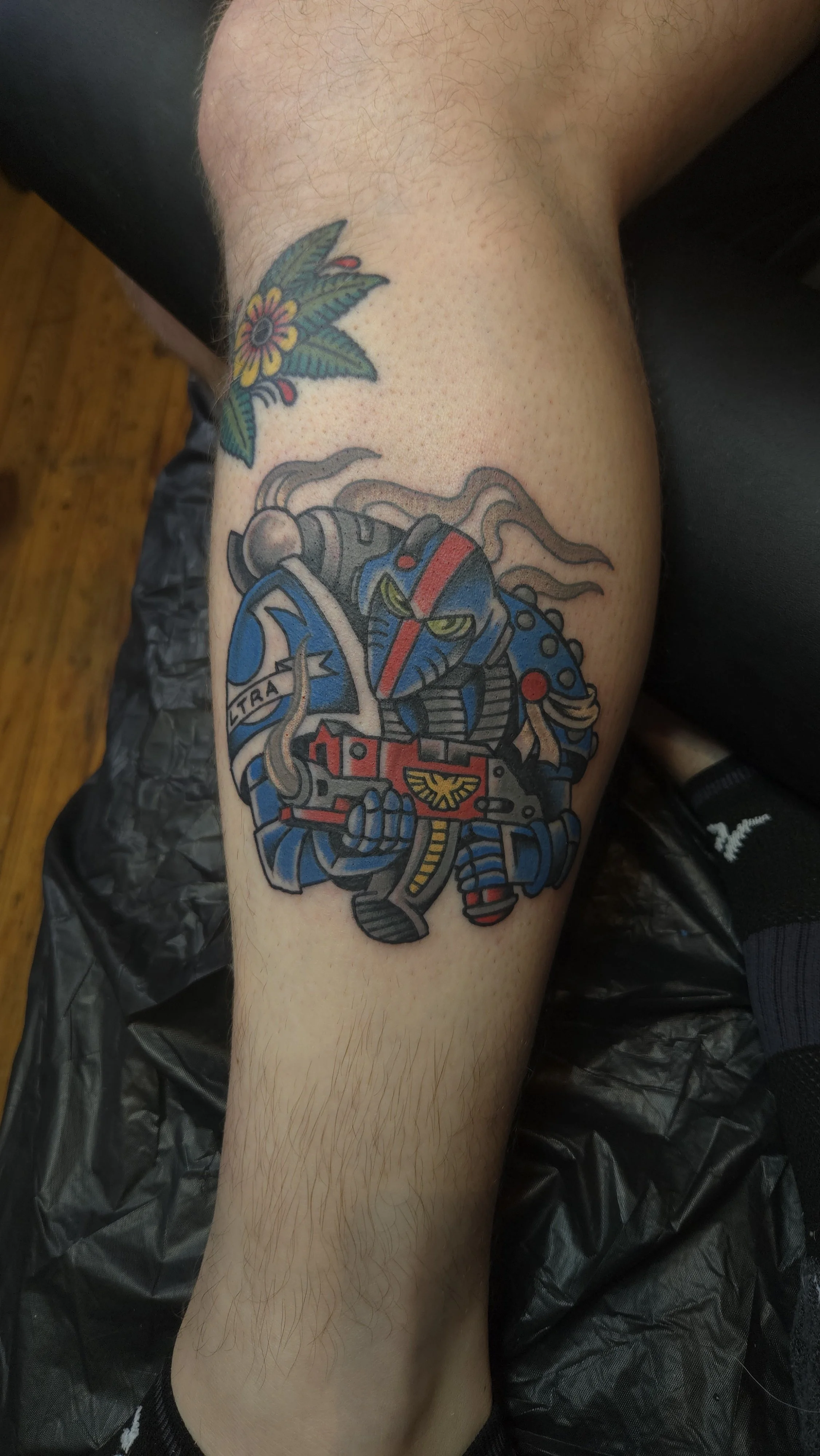 Tattoo of an Ultramarine in Mk VI armor from the Horus Heresy. The marine is blue, holding a bolter with red casing. The bolter is smoking as if freshly unloaded.