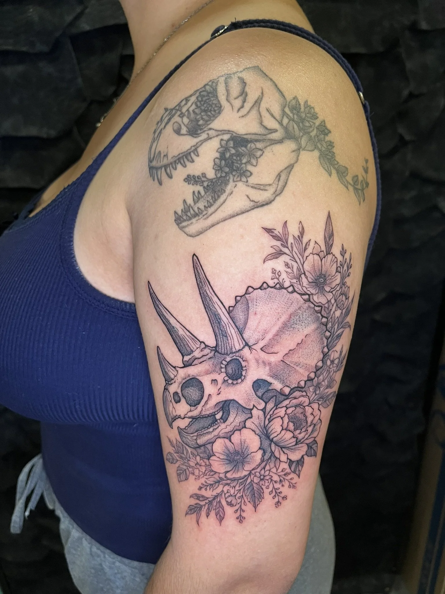 Triceratops skull and flowers in black and grey on an arm