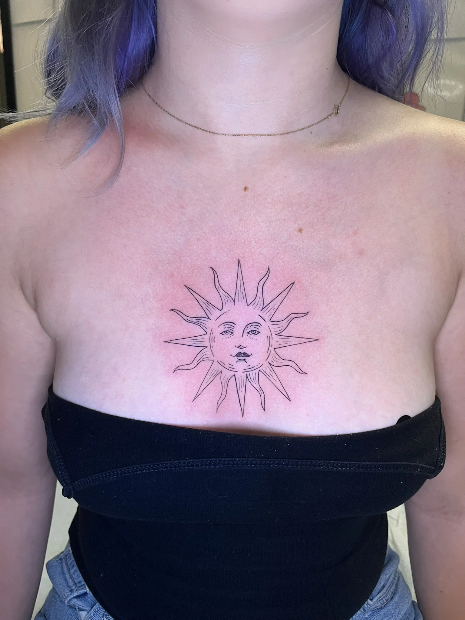 Line work of a medieval style sun in the center of a woman's chest