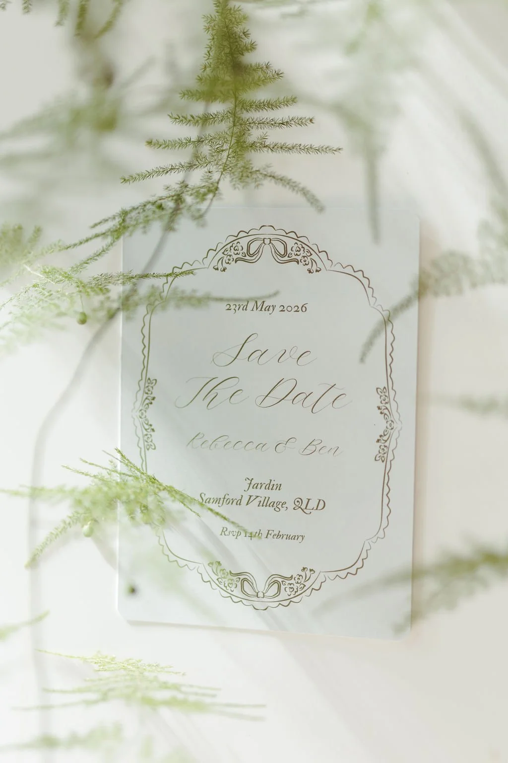 A wedding 'Save the Date' card with elegant gold border design, surrounded by green fern leaves, announcing the wedding of Rebecca and Ben on May 23rd, 2026, at Jardin, Samford Village, with RSVP by February 14th.