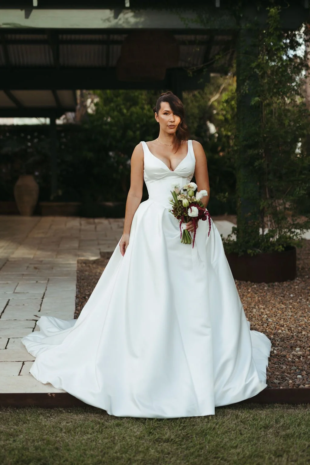 A woman in a white wedding dress holding a bouquet of flowers outdoors.