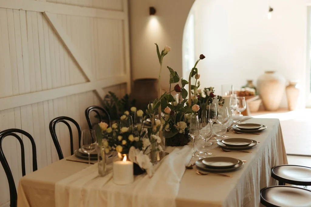 Elegant dining table with floral centerpieces, glassware, plates, and candles in a bright, minimalist room.