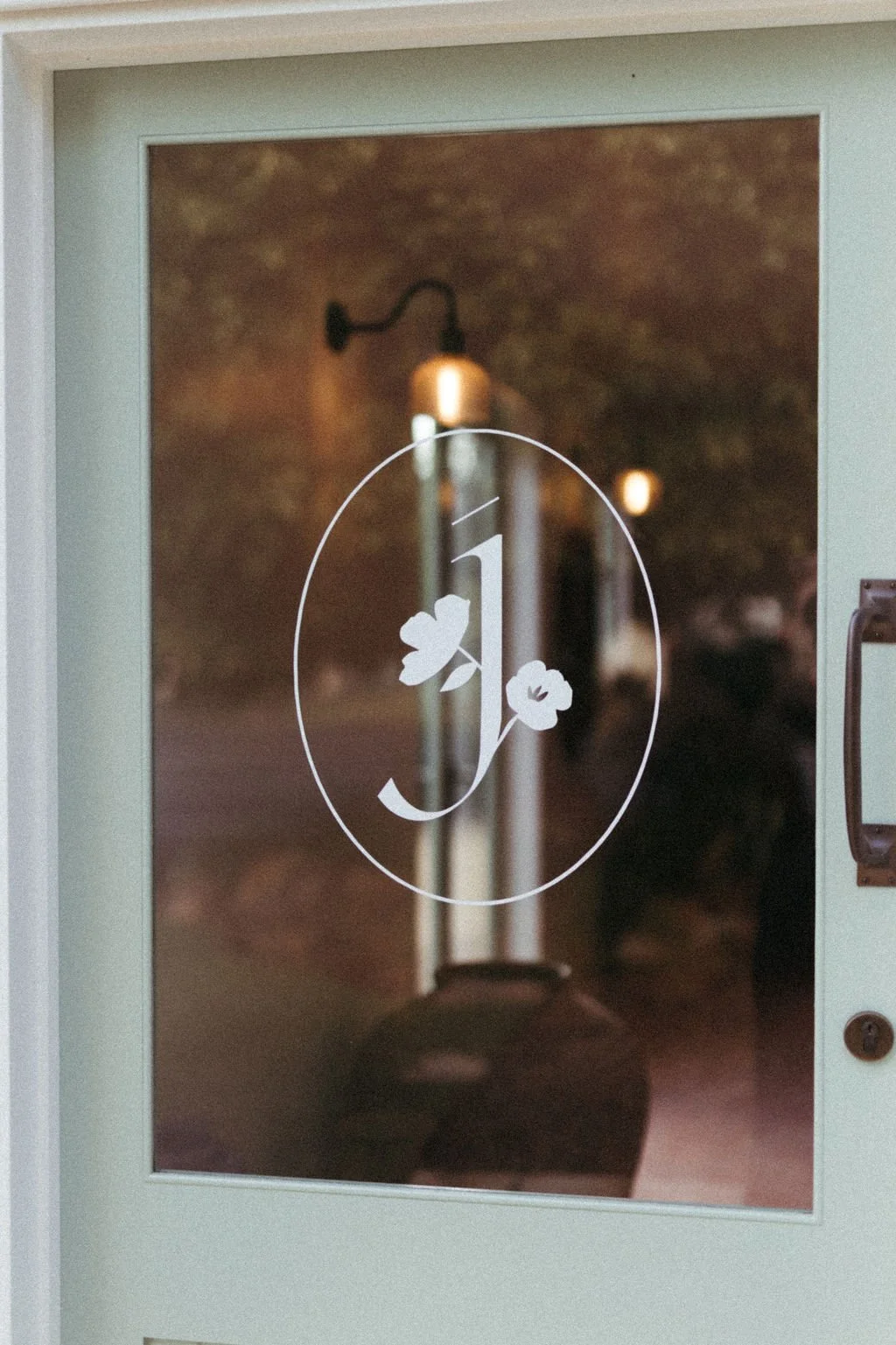 Glass door with a white letter "J" and two flower illustrations, possibly at the entrance of a business or home.