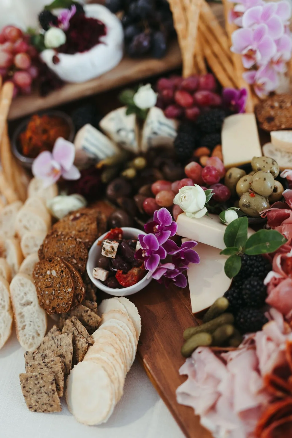 A cheese and charcuterie board featuring grapes, flowers, crackers, and various cheeses.
