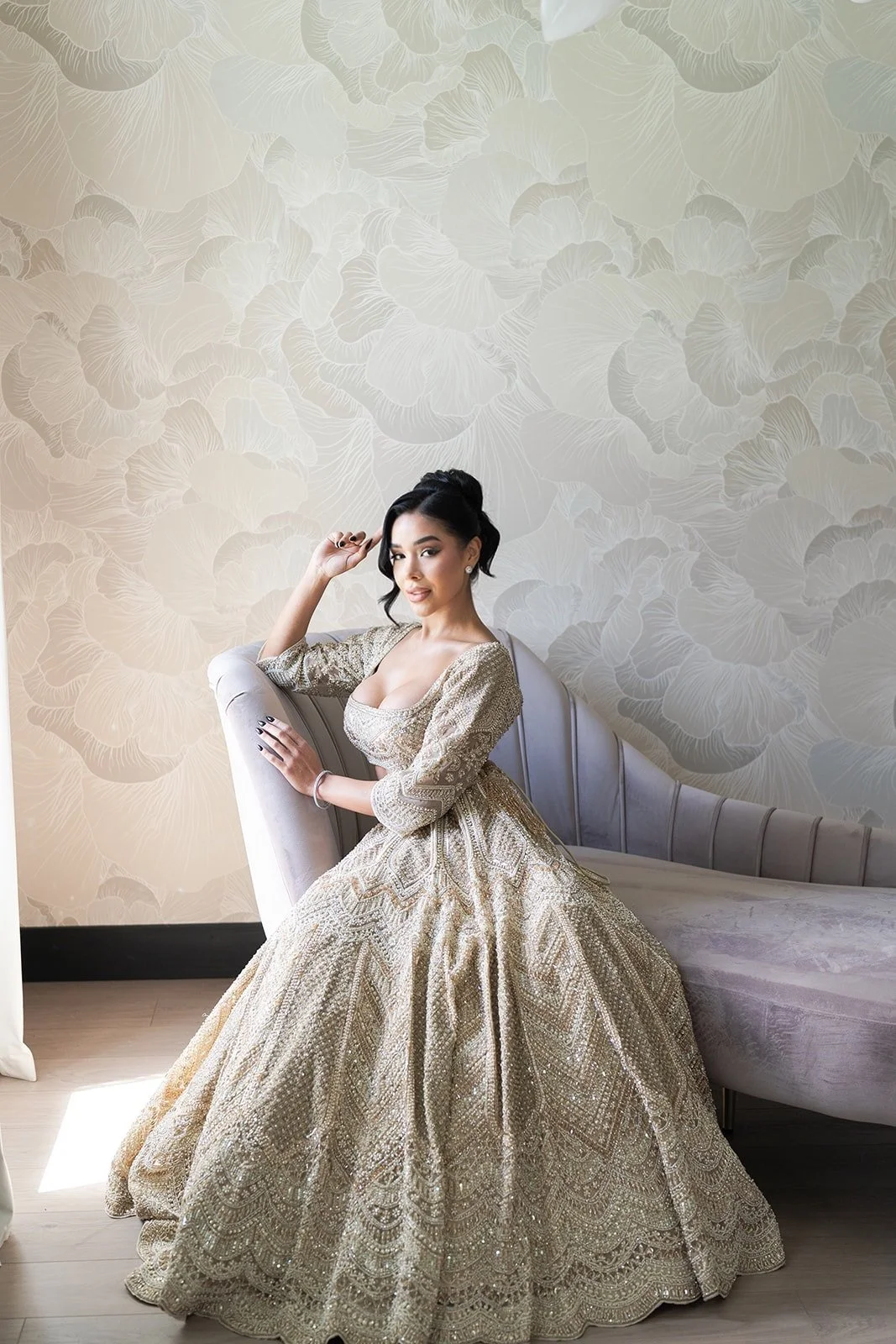 Three women in wedding dresses sitting on a yellow couch in a brightly lit room with modern wall decor.