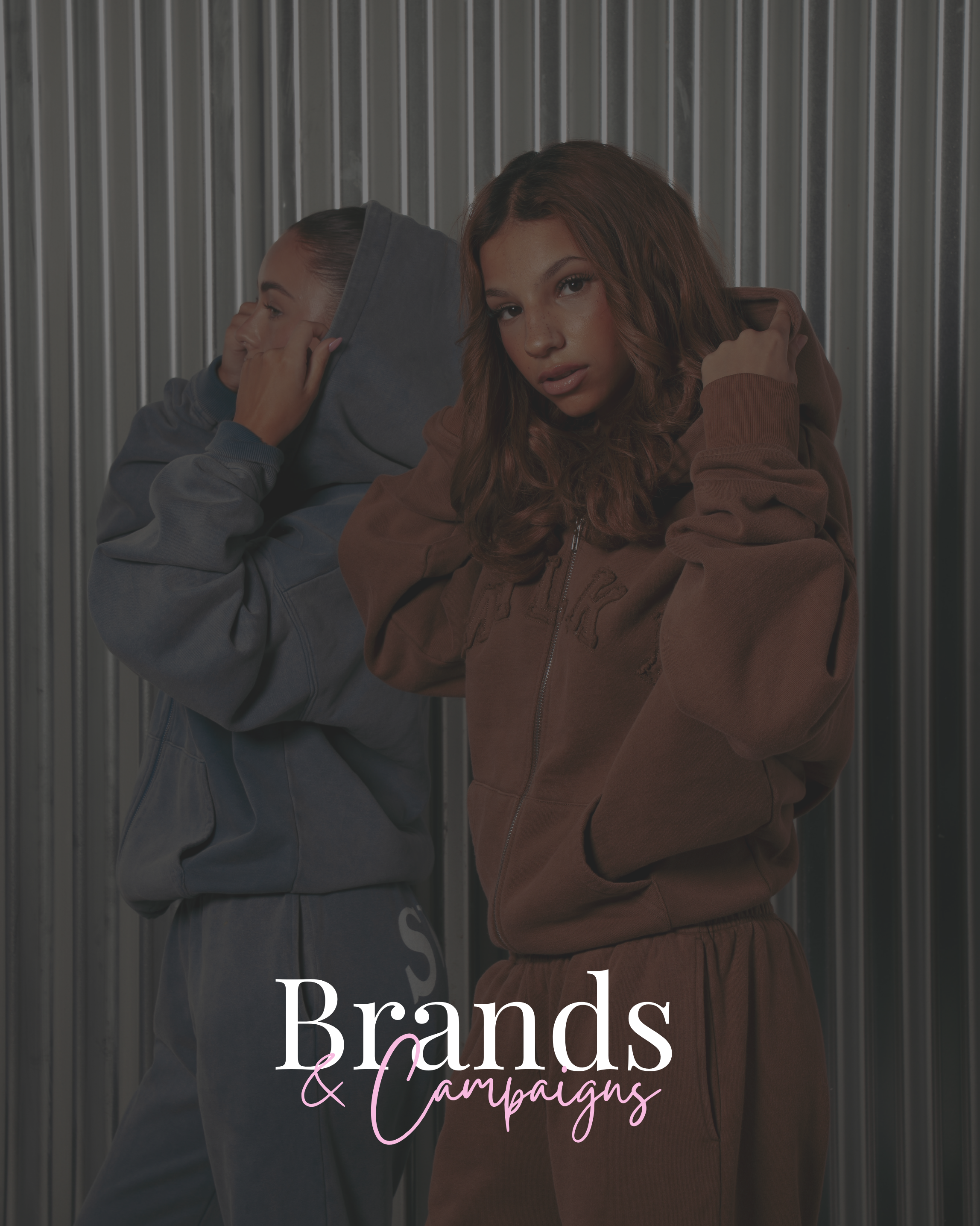 A young woman with brown wavy hair wearing a brown hoodie and matching sweatpants standing in front of a metal wall, with a young girl in a gray hoodie and sweatpants covering her ears in the background. The text overlay says "Brands & Campaigns" in white and pink cursive font.