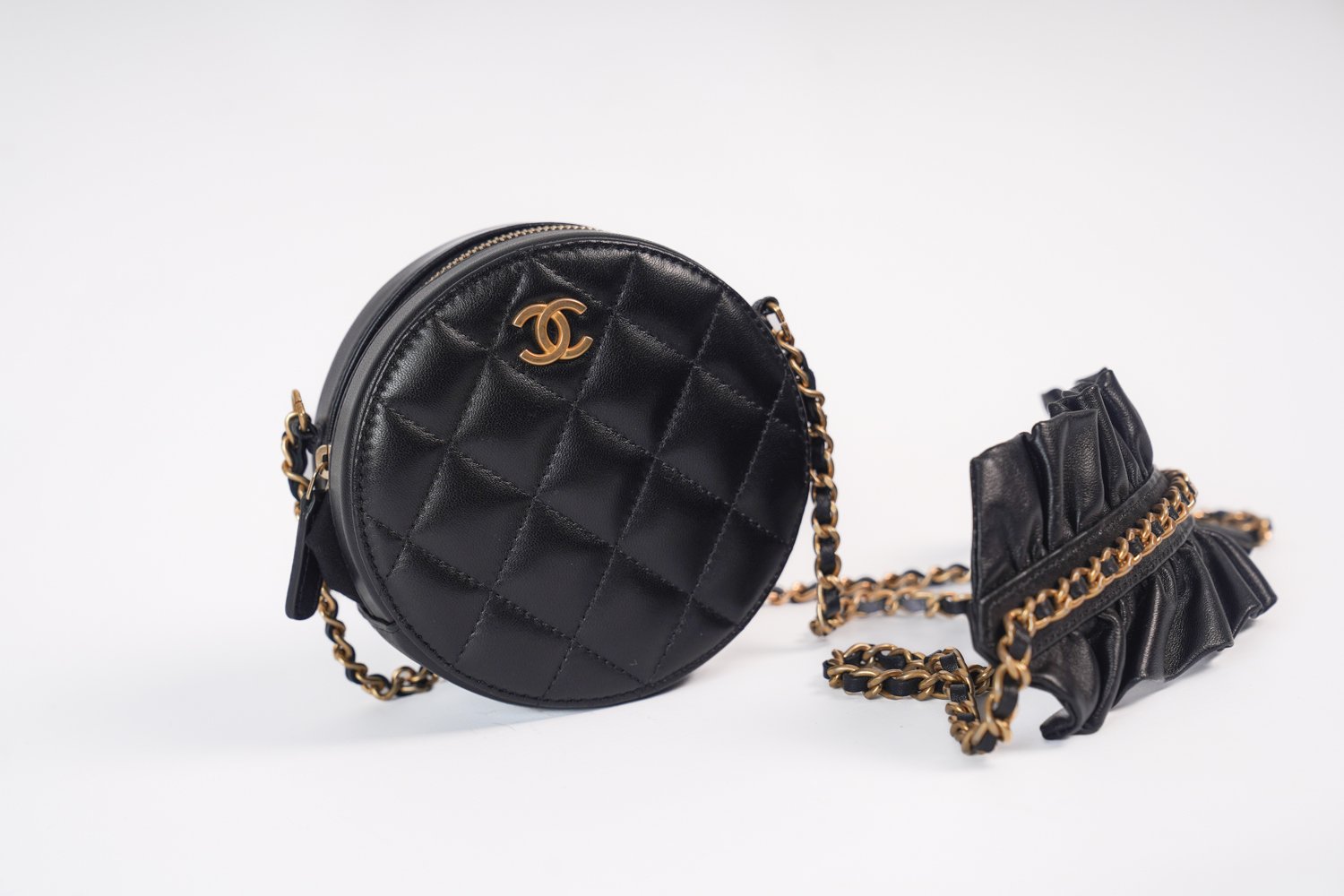 Black quilted leather circular handbag with gold Chanel logo and chain strap, next to a matching smaller clutch purse with ruffled design and gold chain strap.