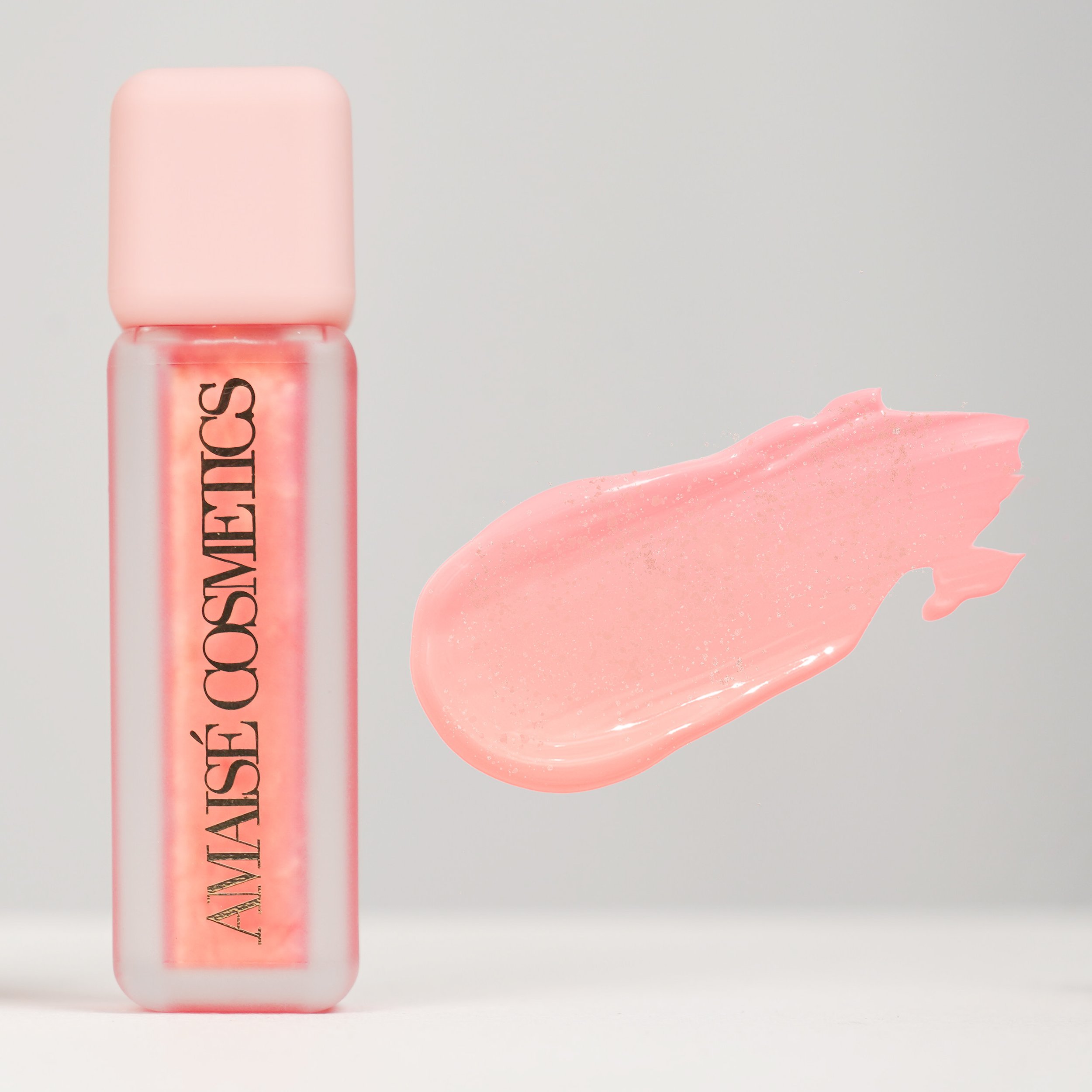 A pink tube of makeup product with a swatch of pink gloss or lipstick next to it on a white background.