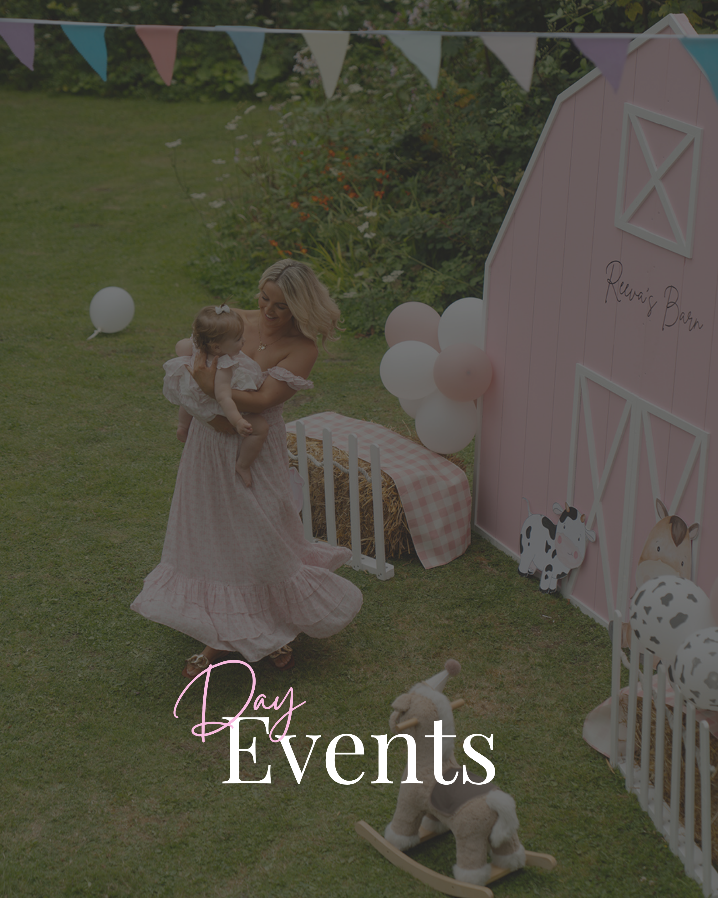 A woman holding a young girl at a farm-themed birthday party with pink barn, animals, balloons, and colorful bunting.