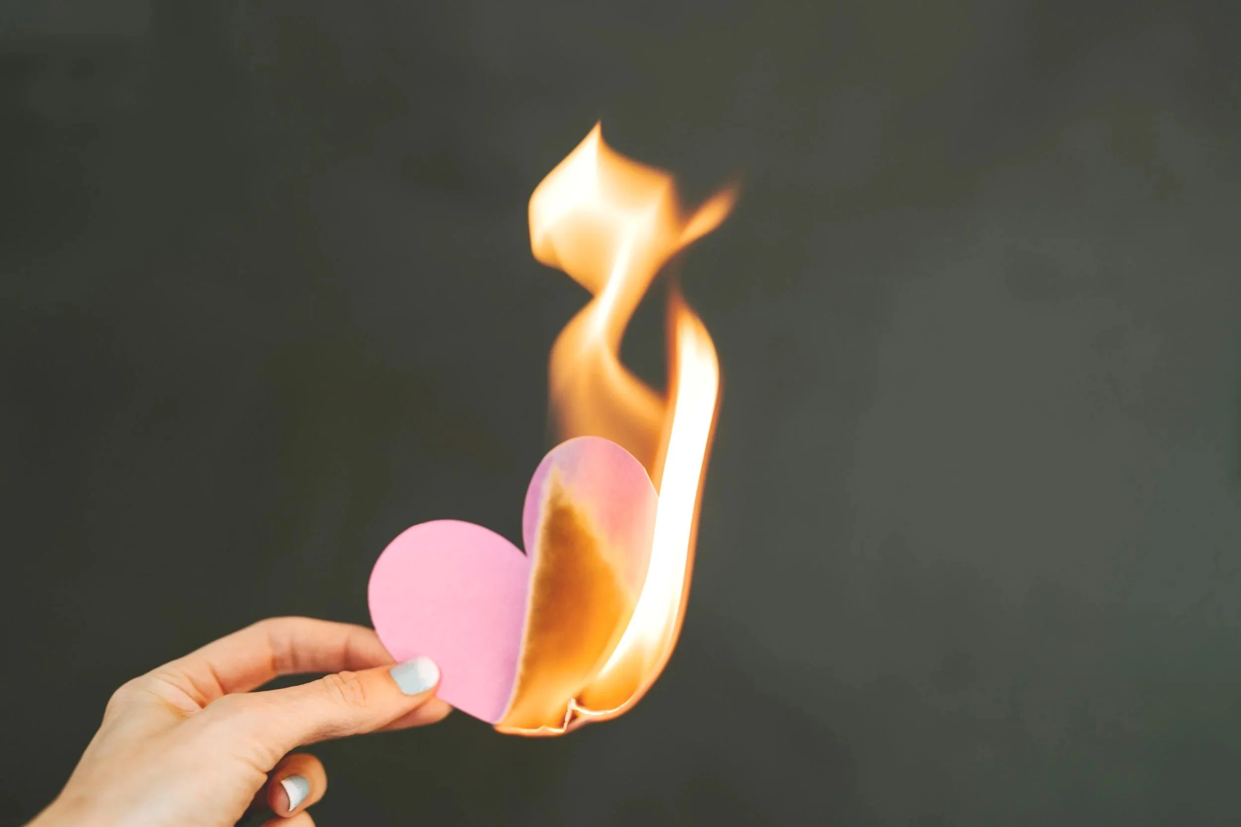 Hand holding burning heart representing heartbreak grief and healing after divorce and relationship loss through attachment based telehealth therapy in Colorado and Iowa