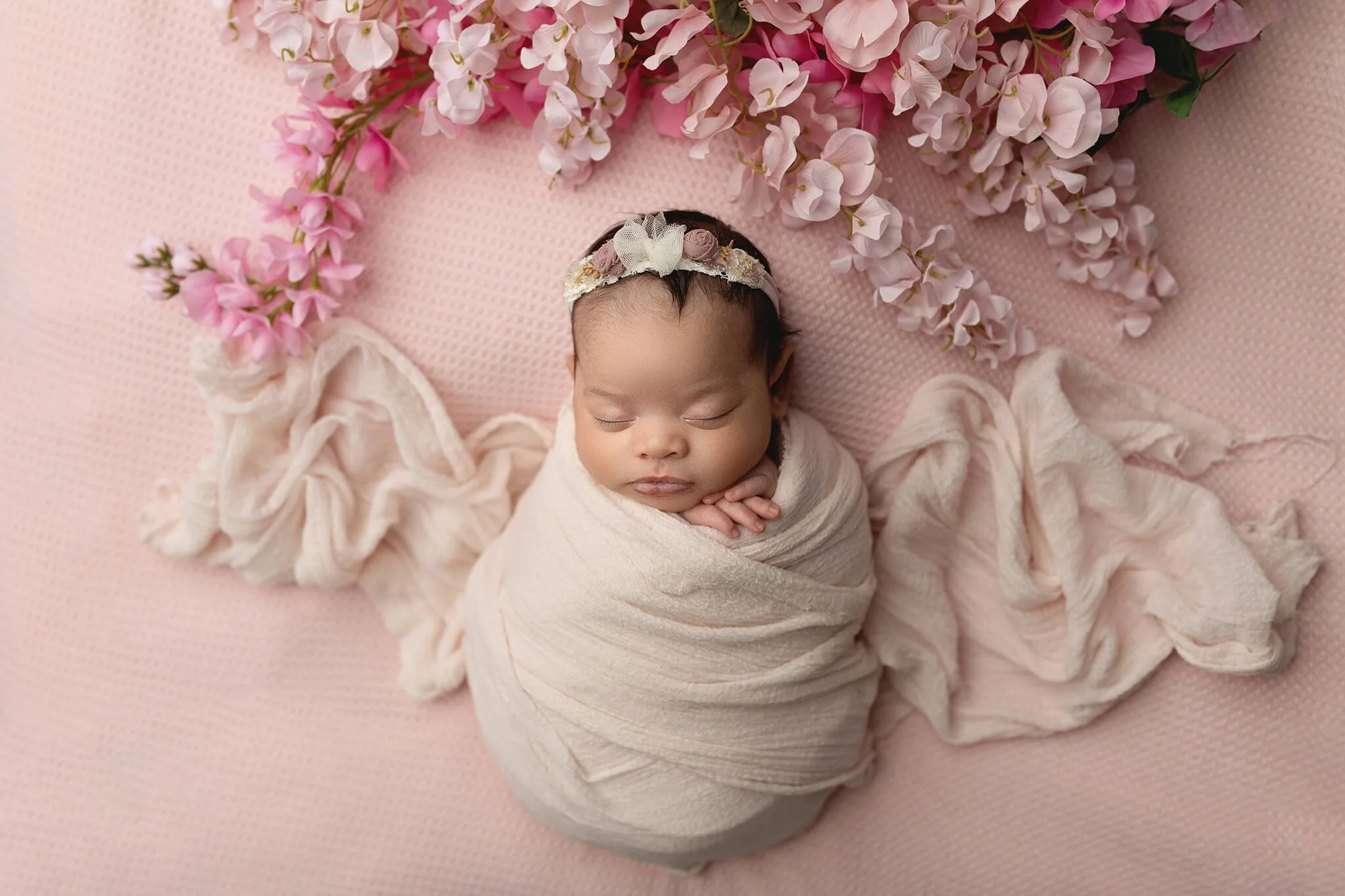 BABY WRAPPED WITH HEADBAND ON, SURROUNDED BY PINK FALLING FLOWERS