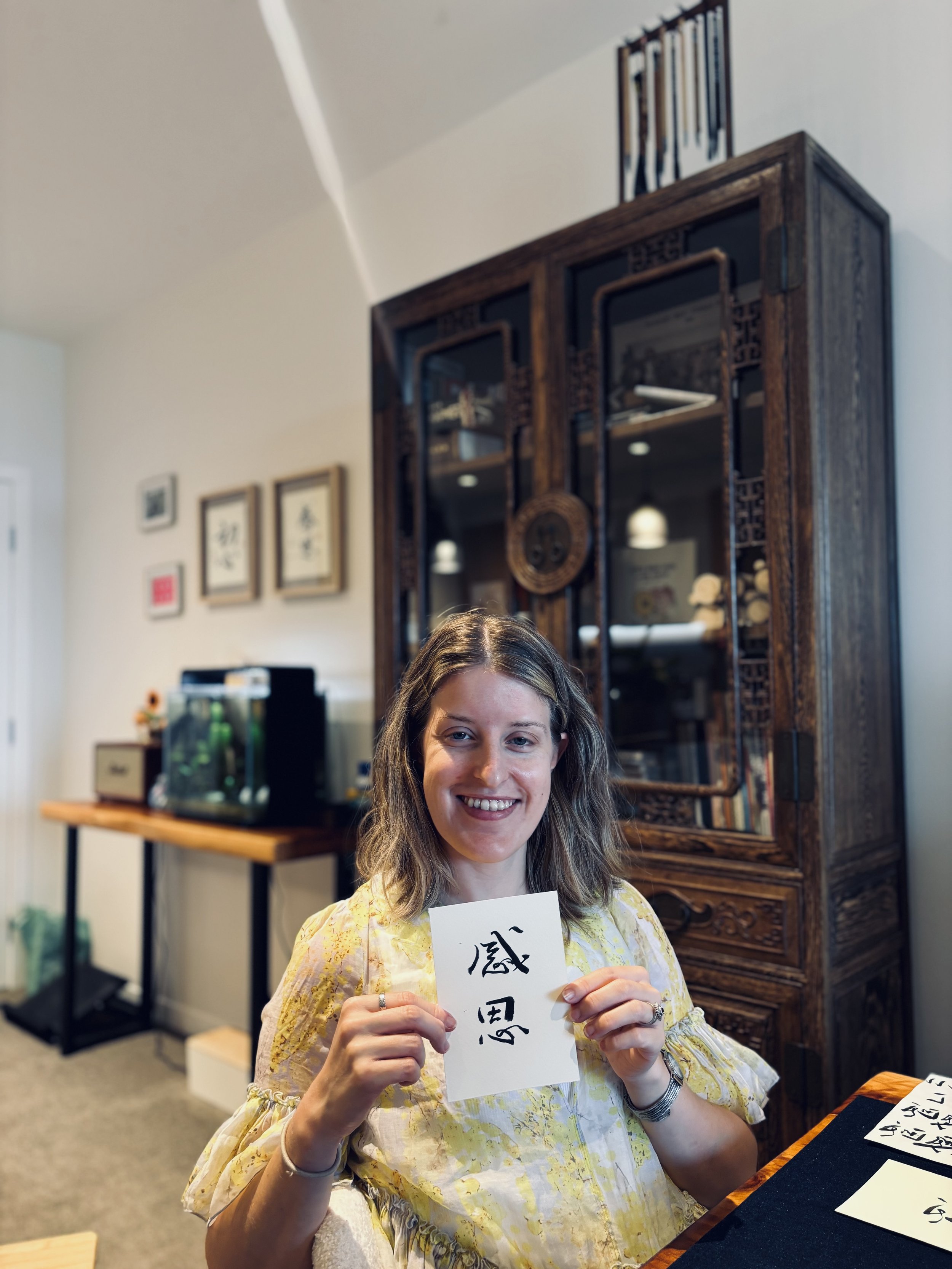 A student smiling and holding chinese calligraphy written on a card