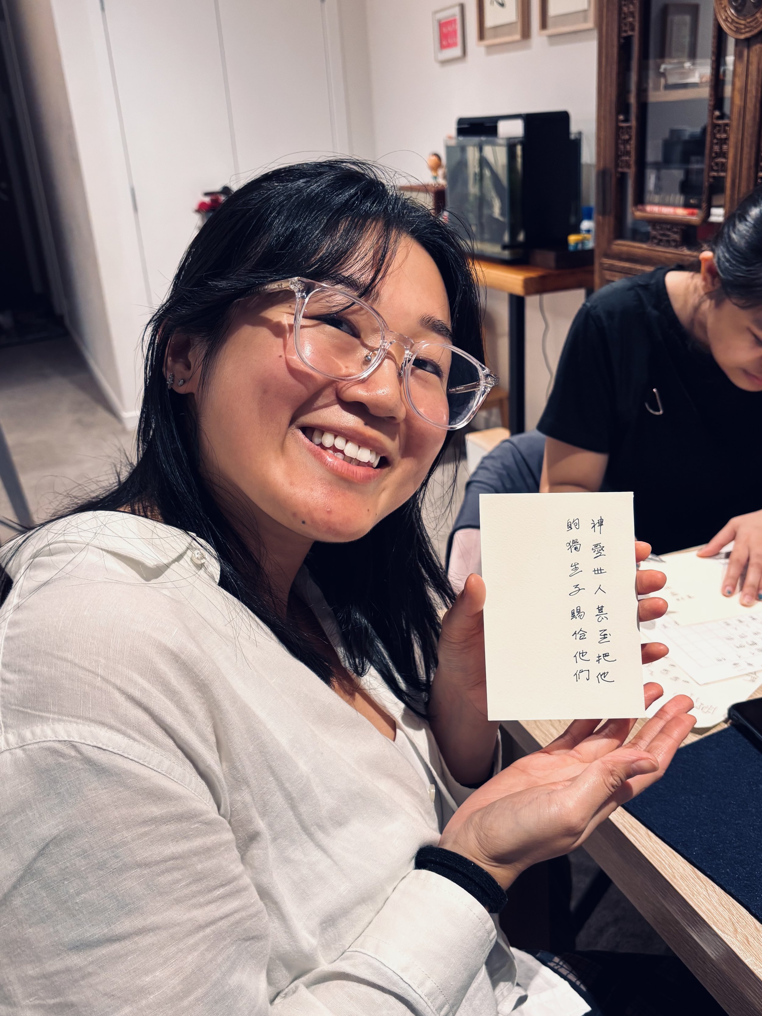 A student smiling and holding Chinese calligraphy written on a card