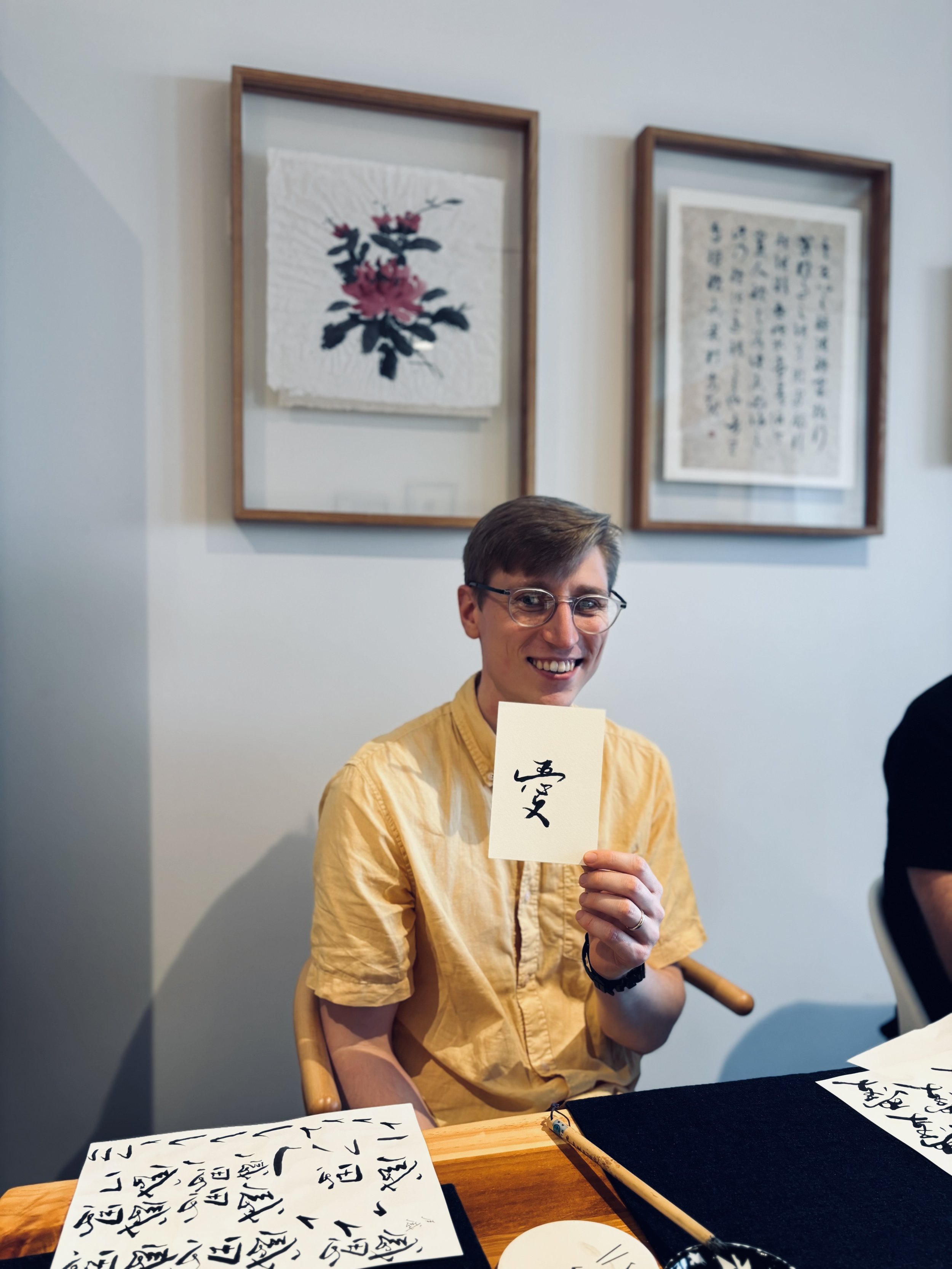 A student smiling and holding a card with Chinese calligraphy