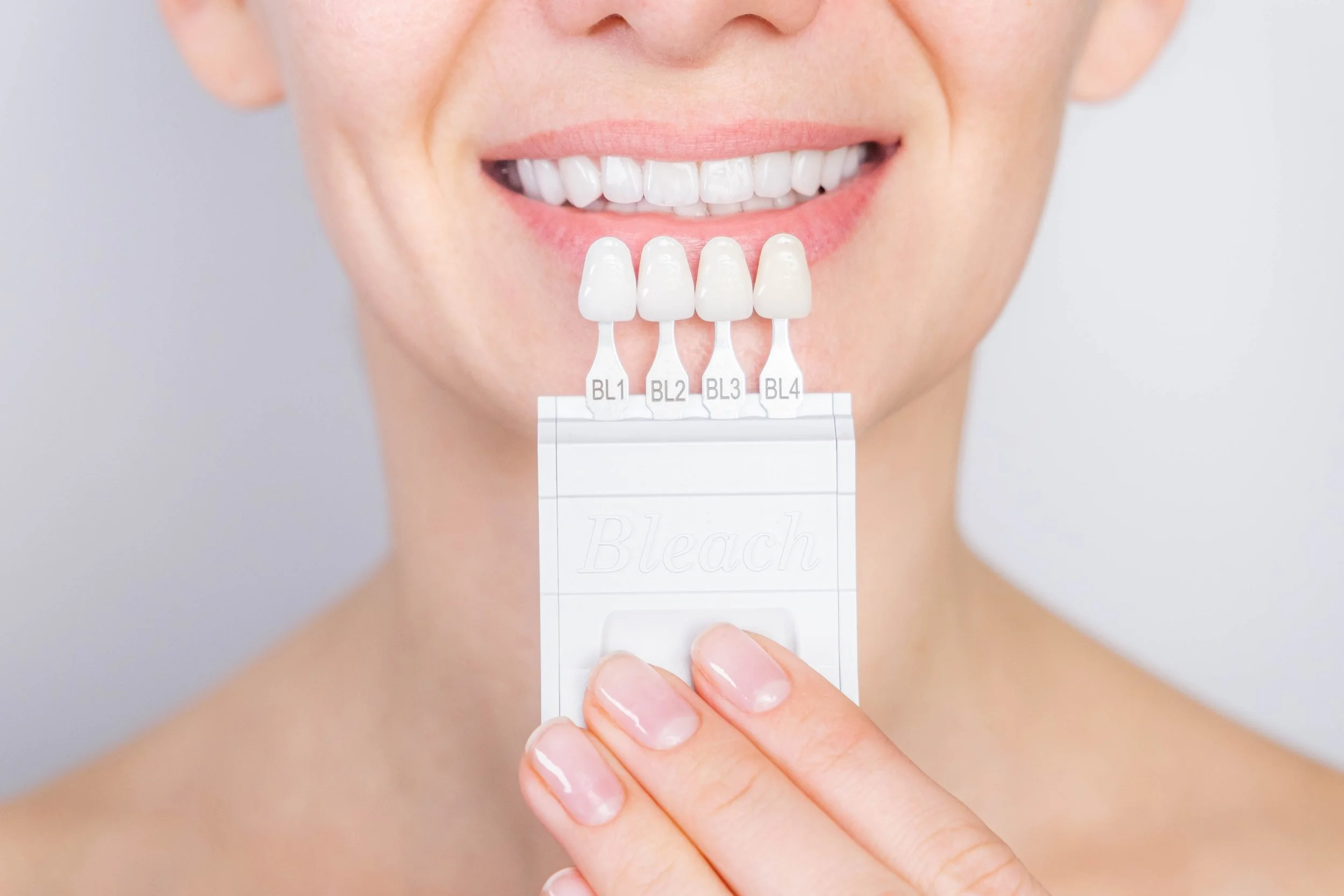 Close-up of a person comparing their teeth with a dental shade guide labeled BL1 to BL4 for tooth whitening.