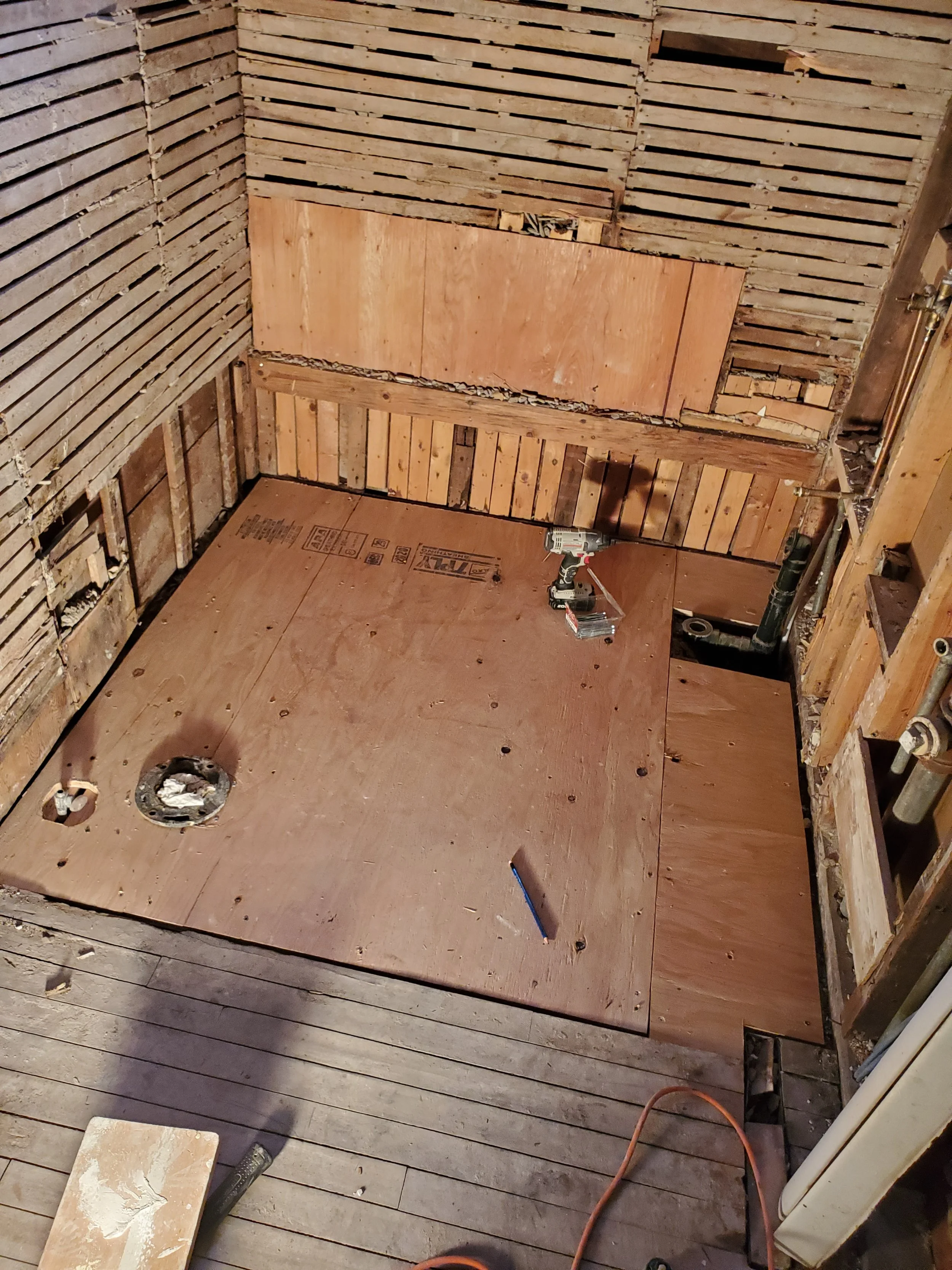 Bathroom under renovation with plywood flooring and partial wall framing.