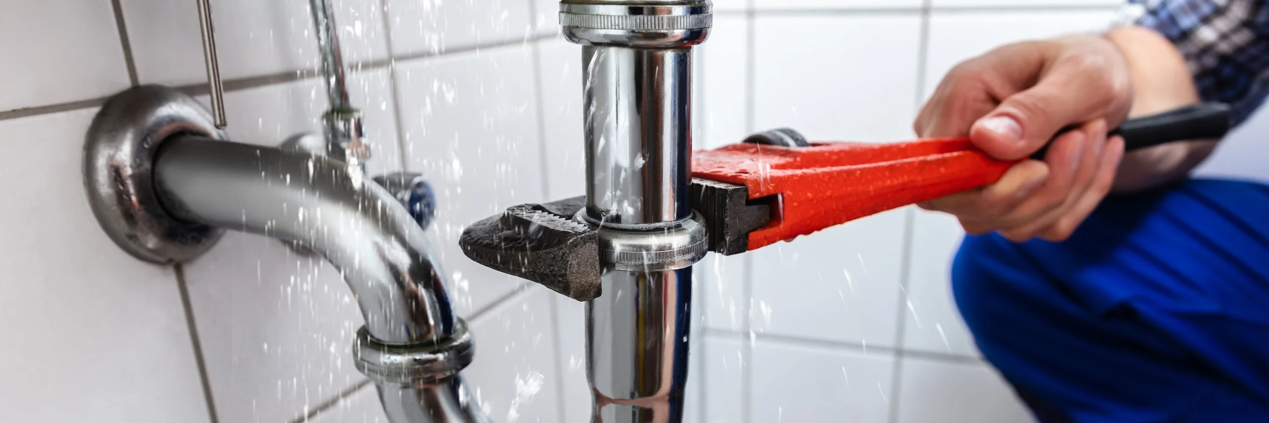 A person using a pipe wrench to tighten or loosen plumbing under a sink, with water flowing from the faucet.