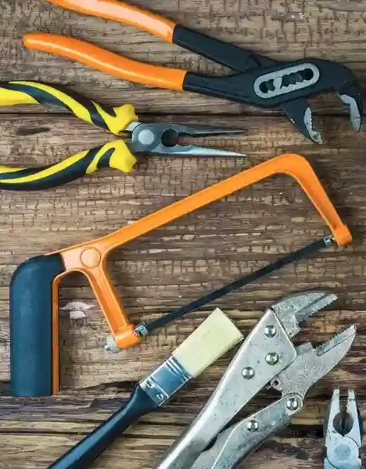 Tools arranged on a wooden surface, including pliers, a hacksaw, a hand saw, a wrench, and a pair of needle-nose pliers.