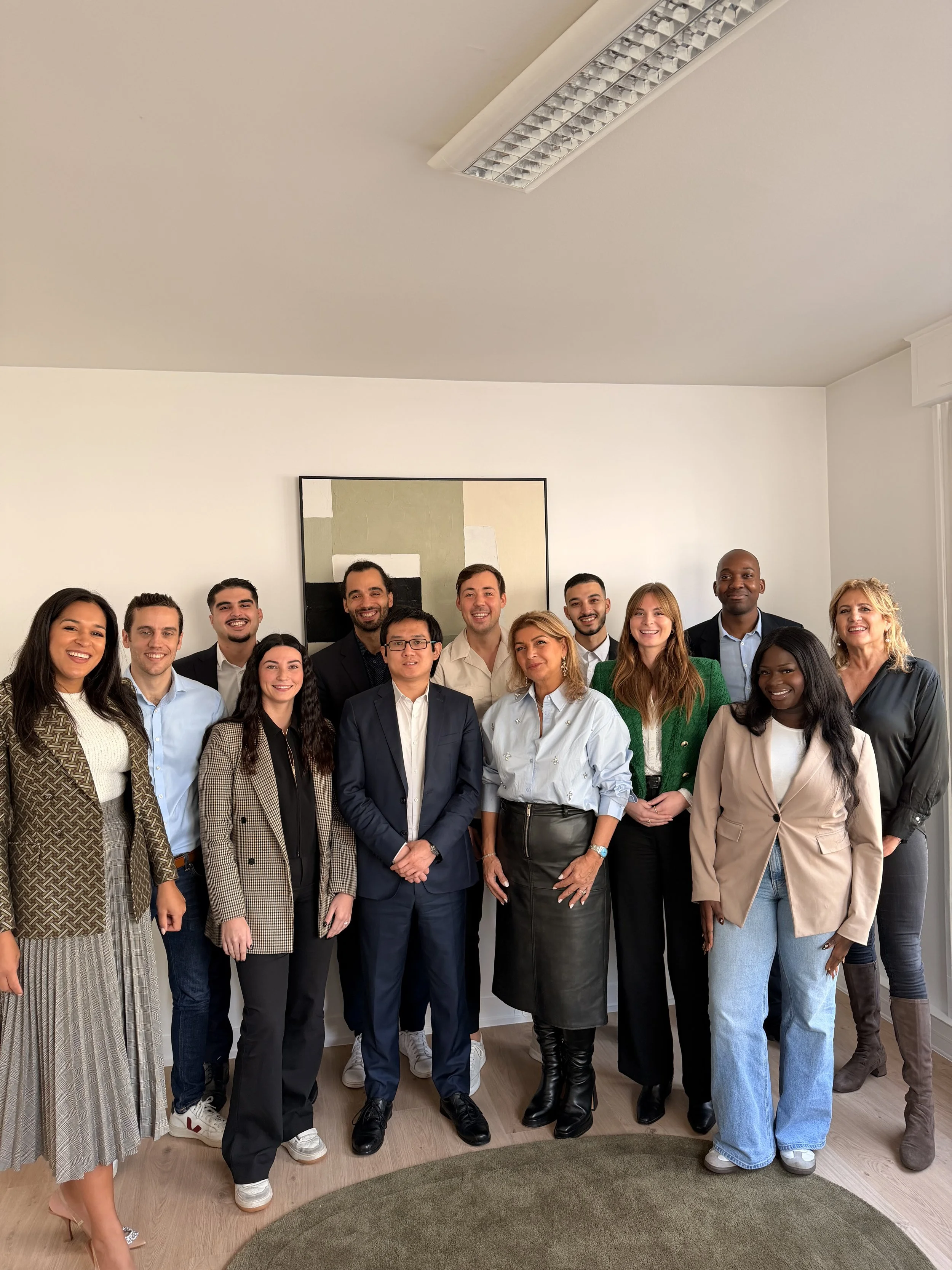 Groupe de quinze personnes posant pour une photo dans une pièce lumineuse avec un tableau abstrait derrière eux.
