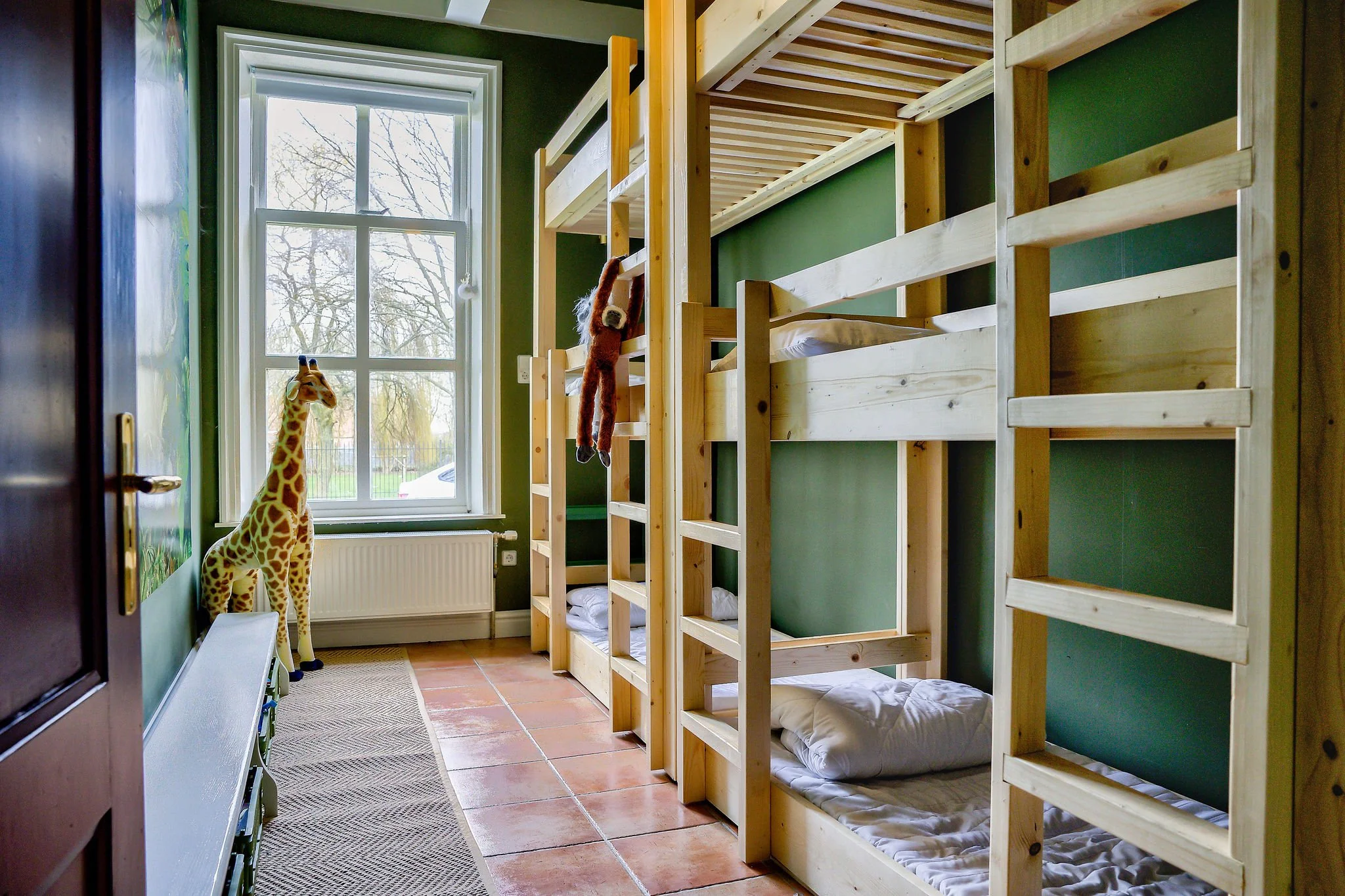 Stapelbedden in een kinderkamer met groen geverfde muren en een groot raam. Een opgezette giraffe en een knuffeldier hangen aan het bed.