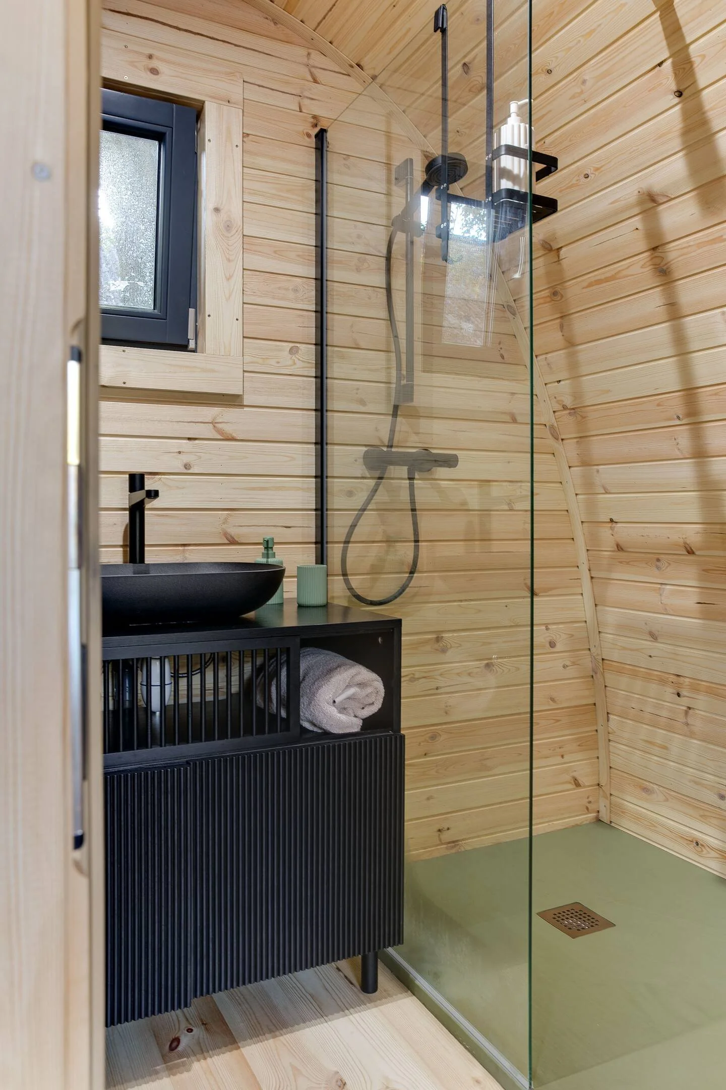 Moderne badkamer met houten wanden, een zwarte wastafel en kast, een glazen douchewand, en douchekop.