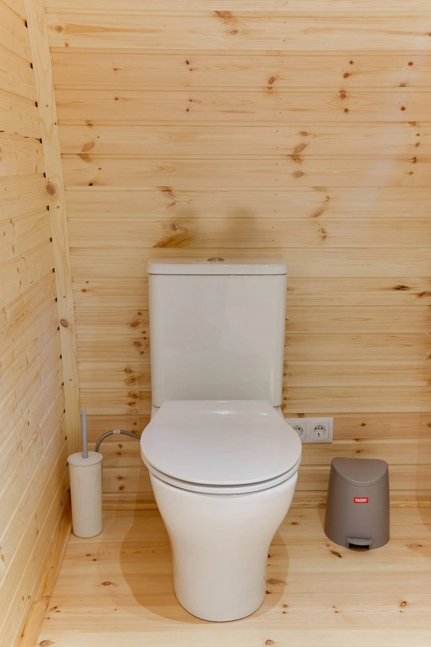 Wit toilet in houten badkamer met toiletborstel en prullenbak.