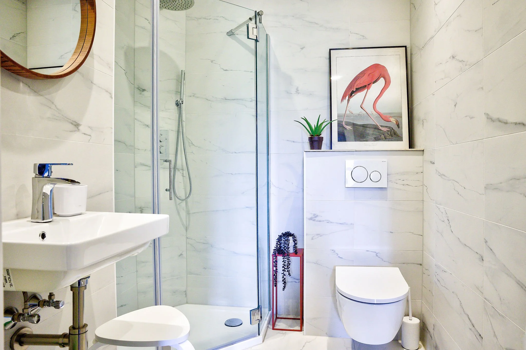 Moderne badkamer met douchecabine, wastafel, toilet en een plant. Er hangt een schilderij van een flamingo aan de muur. Het interieur heeft marmeren tegels.