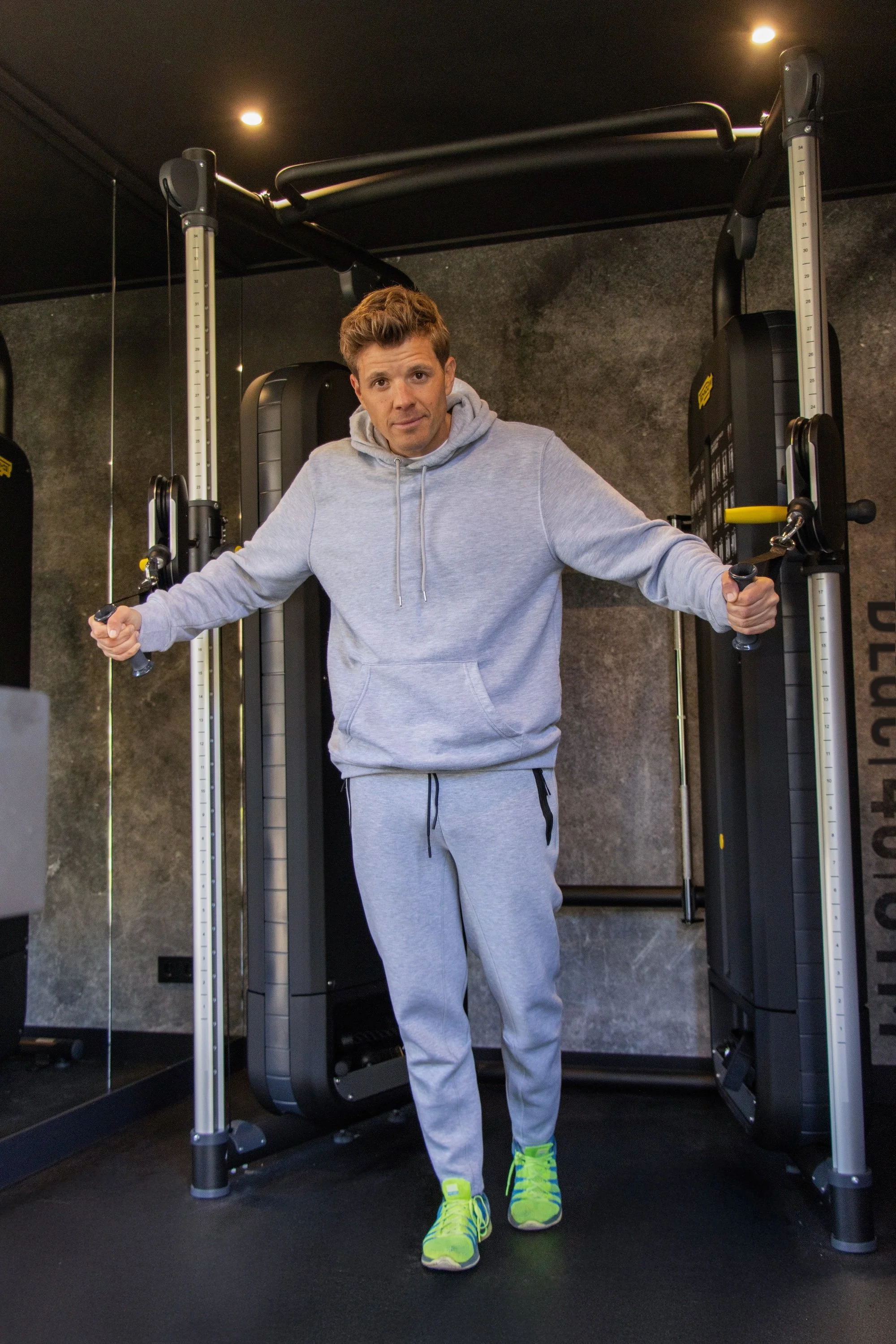 Man traint aan een kabelstation in een 40ft  thuis gym unit met donkere stenen wanden