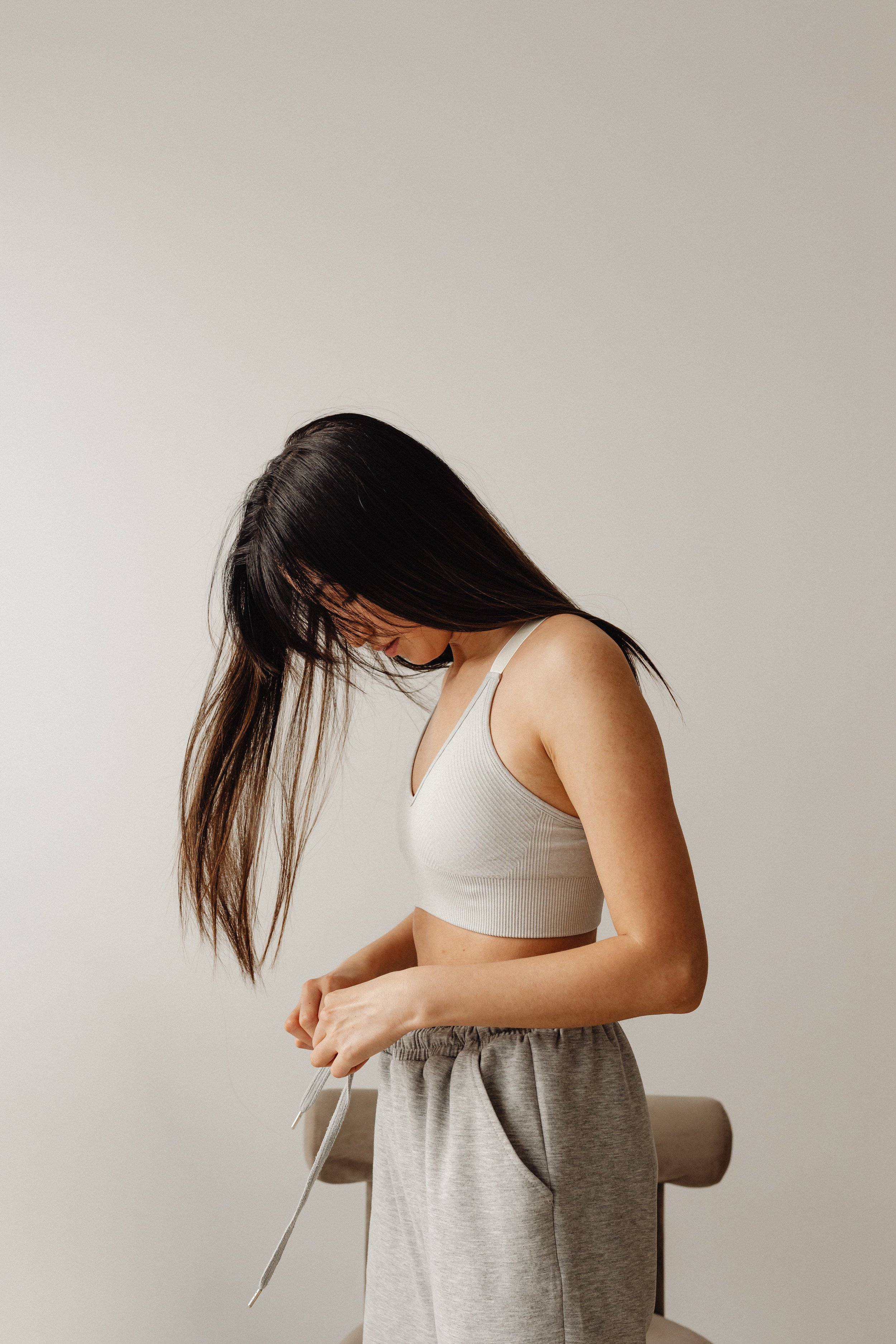 Femme debout sur fond clair qui a la tête penchée vers le sol et les mains près du ventre