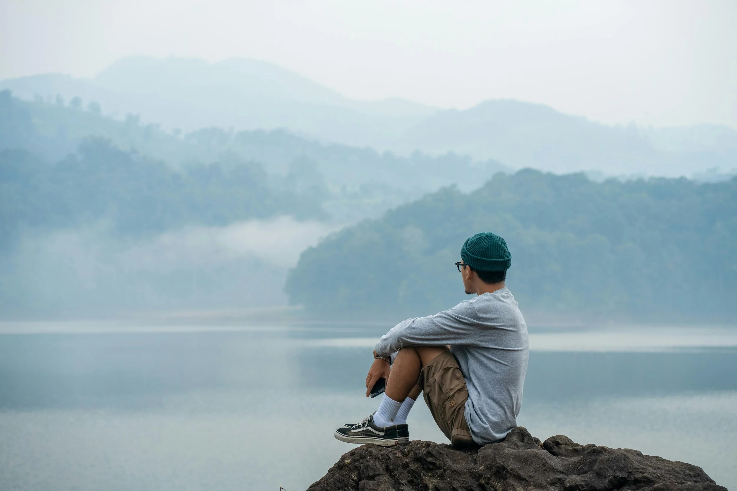 Homme assis sur un rocher devant un lac et des montagnes qui regarder au loin