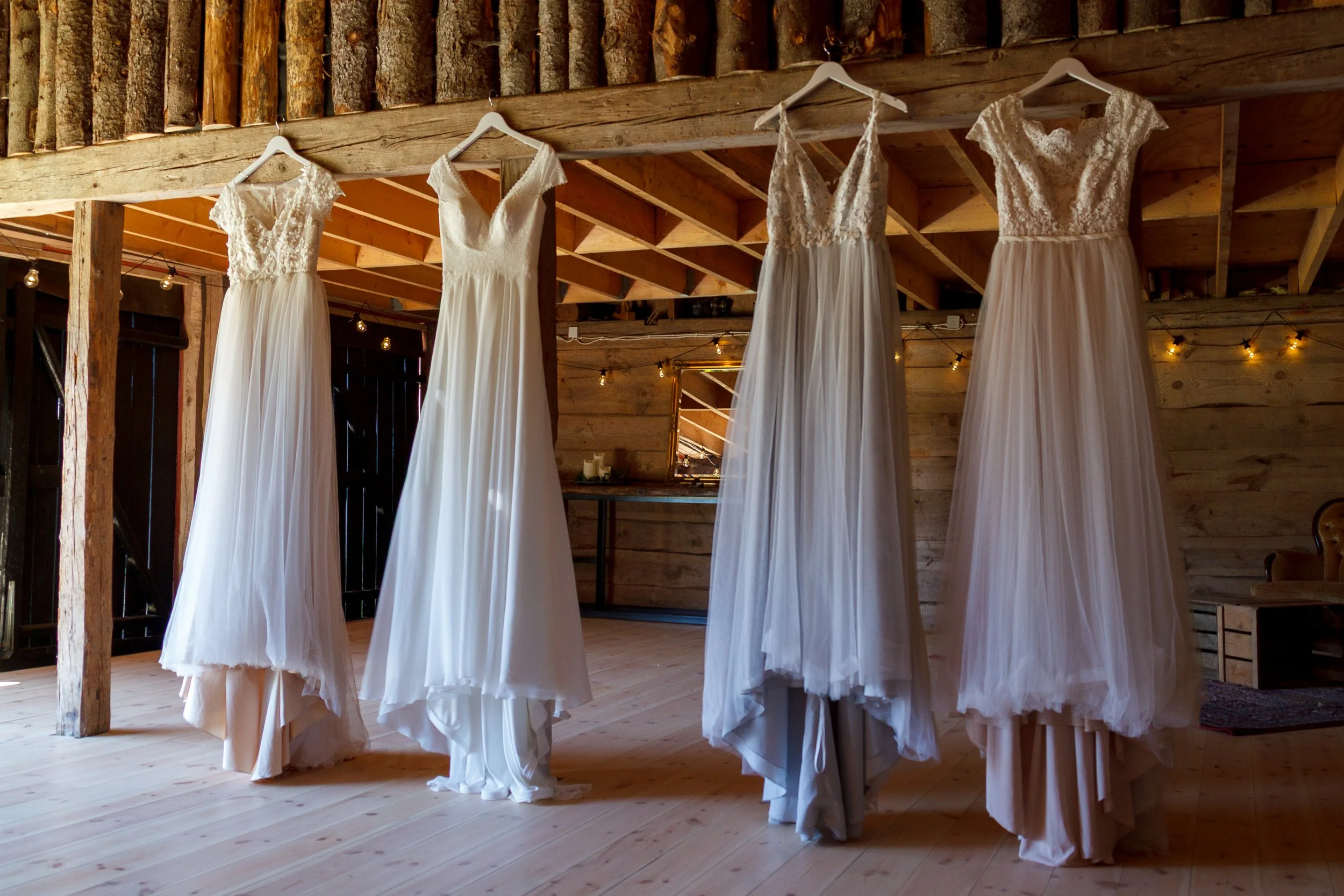 Fyra bröllopsklänningar hängande på krokar i ett träskåp, med ett rustikt trä staket och inomhusdekor i bakgrunden.