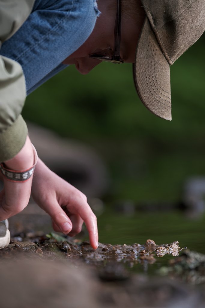 Pojke som böjer sig ner nära vattnet och pekar på något på marken