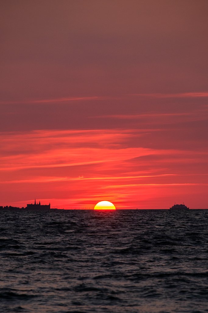 Solnedgång över havet med en stadssilhuett i horisonten, rosa och orangea moln på himlen.