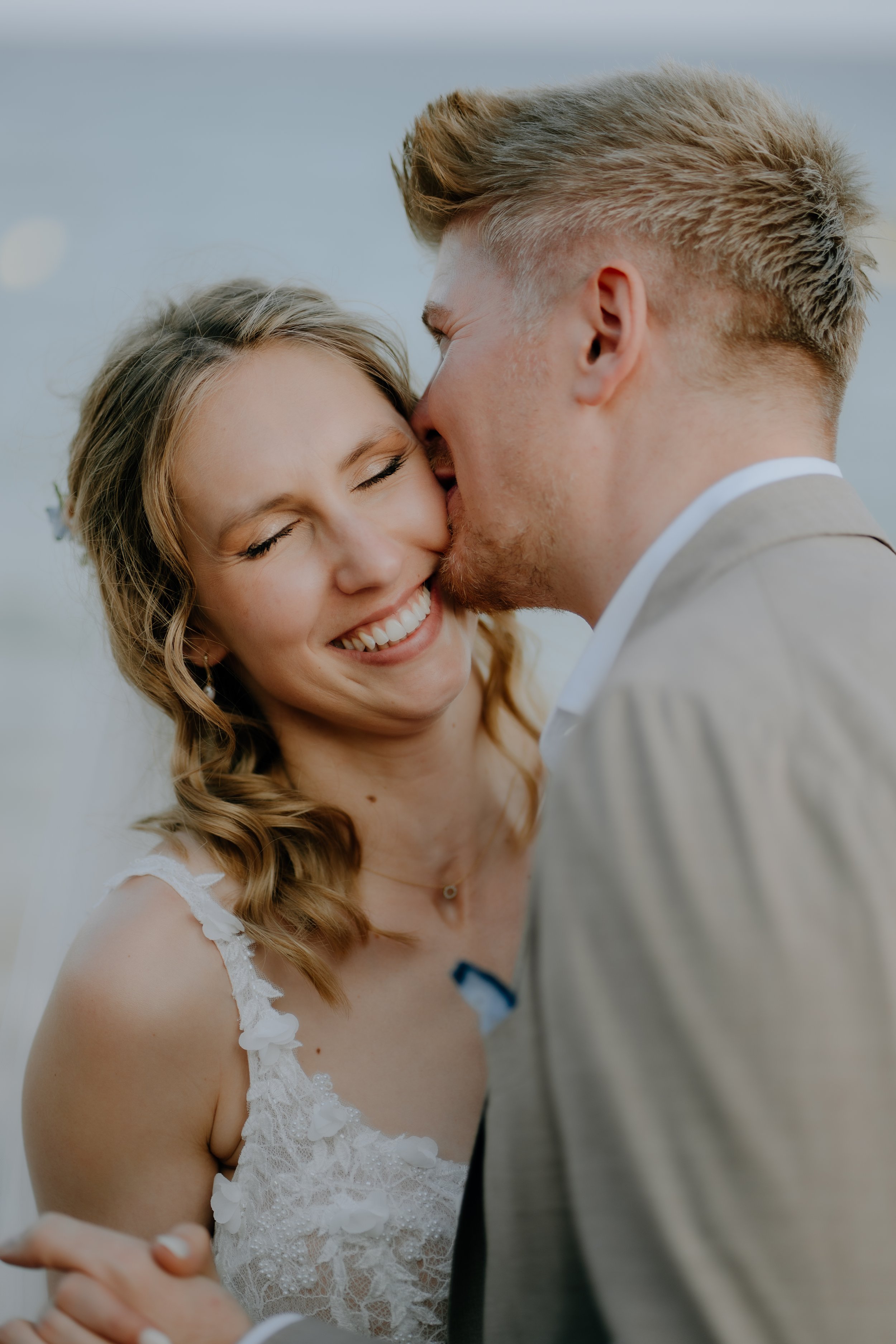 A happy bride and groom sharing a kiss at their wedding, with the bride smiling and the groom kissing her cheek.