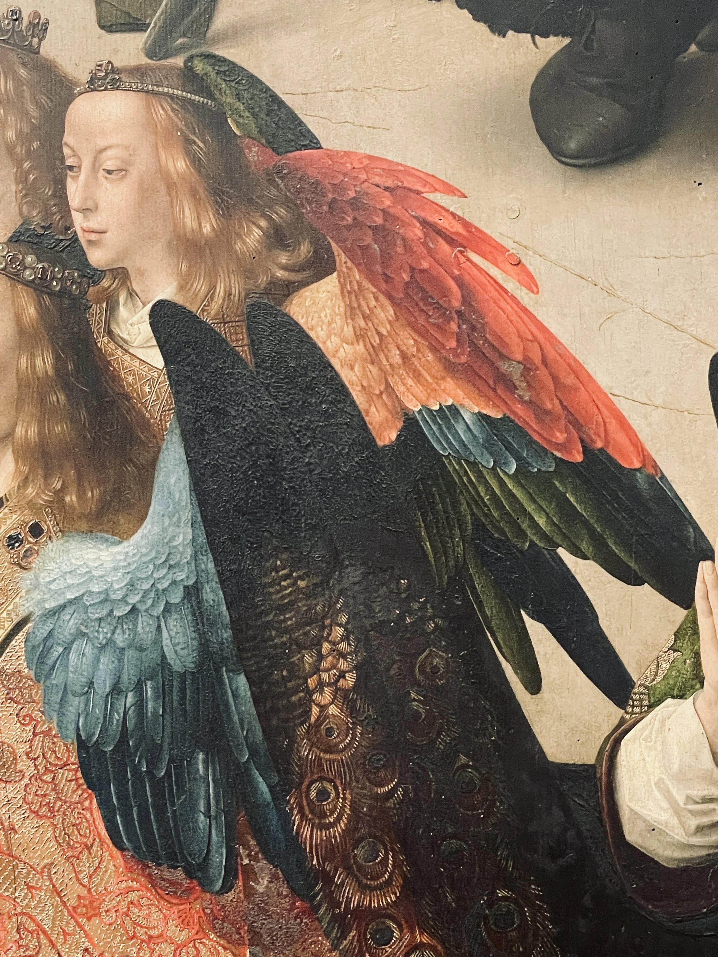 A detailed, colorful artwork of a woman with long hair and a crown, adorned with large, vibrant bird wings in shades of red, orange, green, and blue, and elaborate intricate clothing.