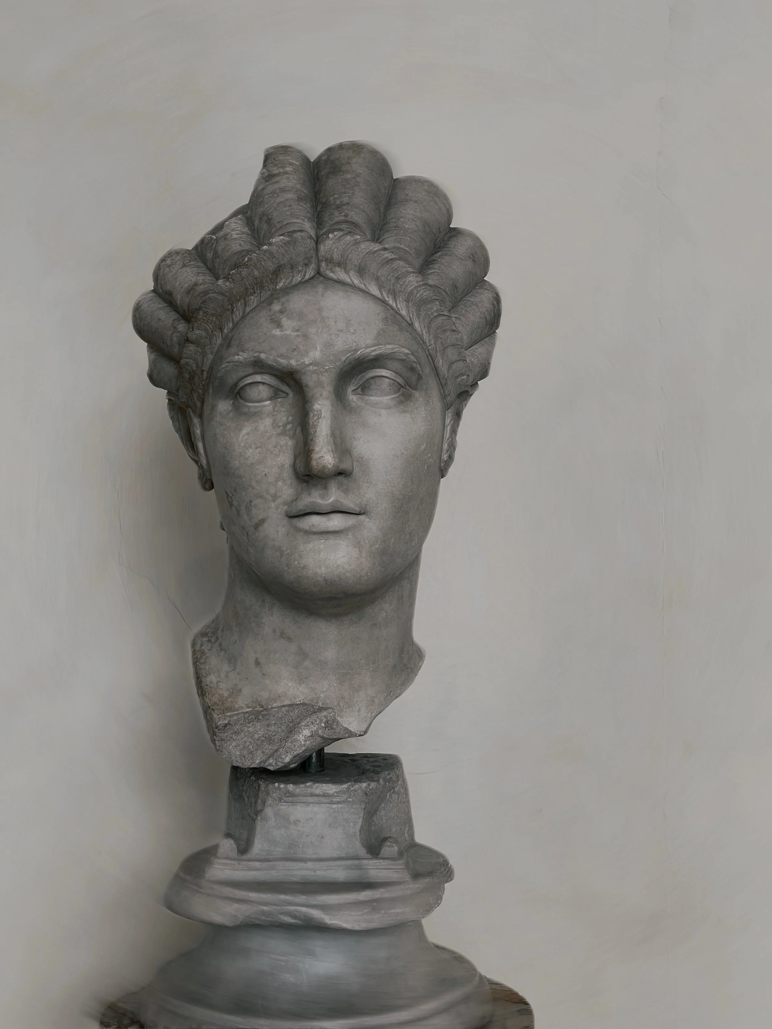 A classical stone bust sculpture of a woman with intricately styled hair, mounted on a pedestal.
