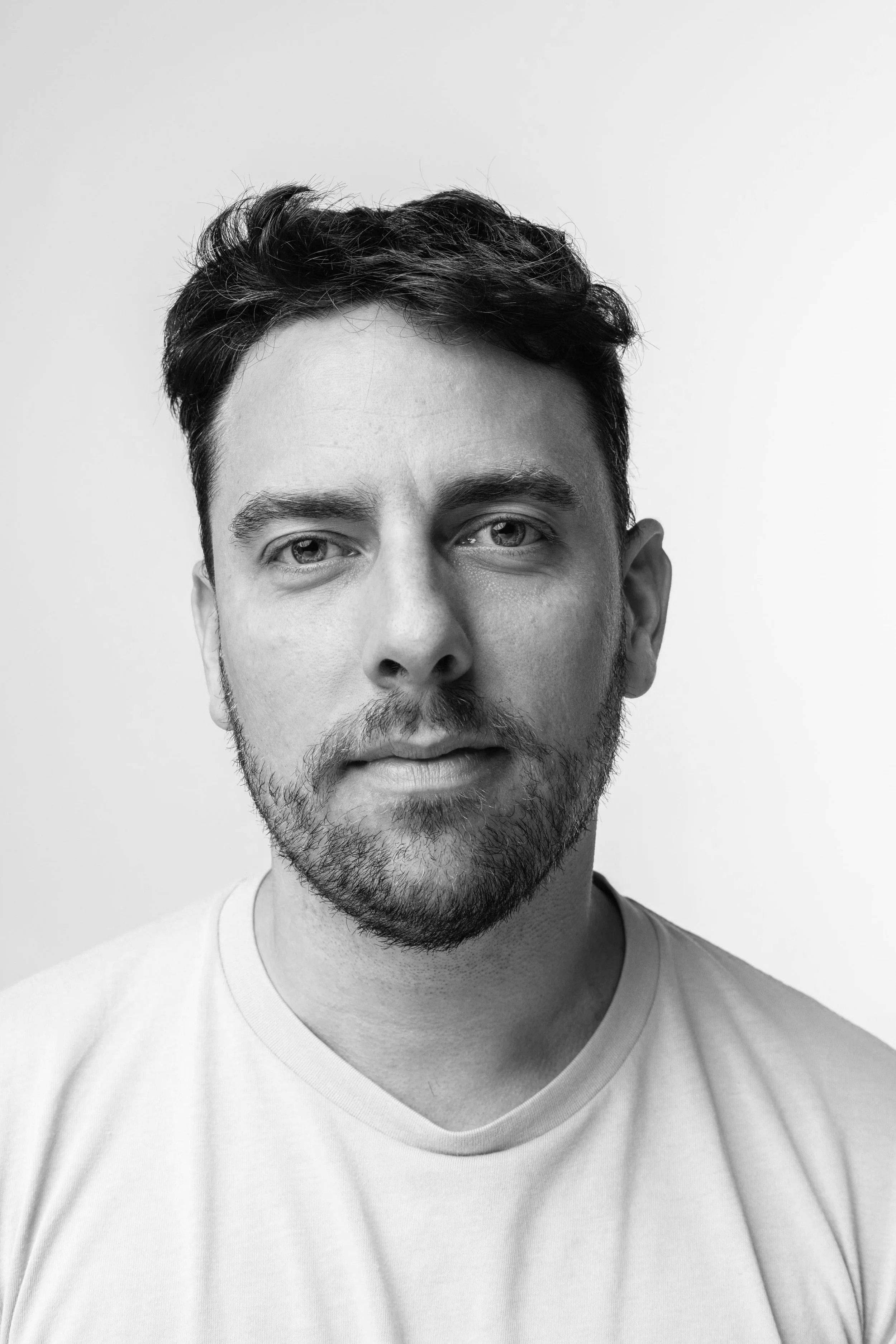 Black-and-white portrait of a young man with short dark hair, facial hair, and a serious expression, wearing a light-colored shirt.