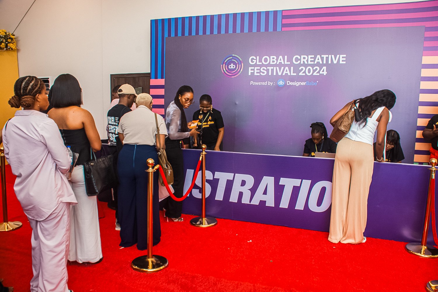 People standing in line at the registration desk for the Global Creative Festival 2024 with a purple banner and red carpet.