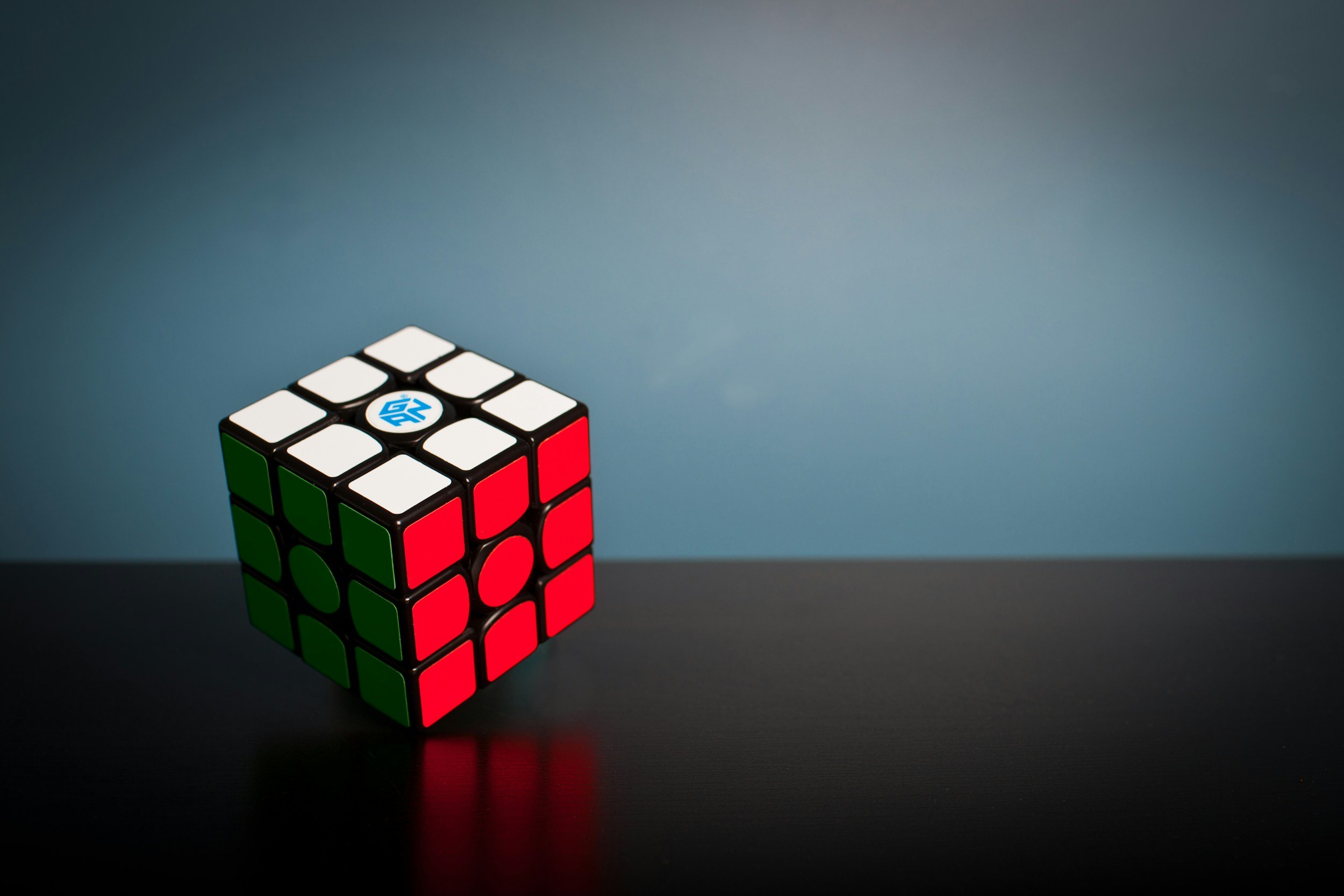 A Rubik's Cube with mixed red, green, white, and black stickers on a dark surface against a background with a gradient of blue shades.