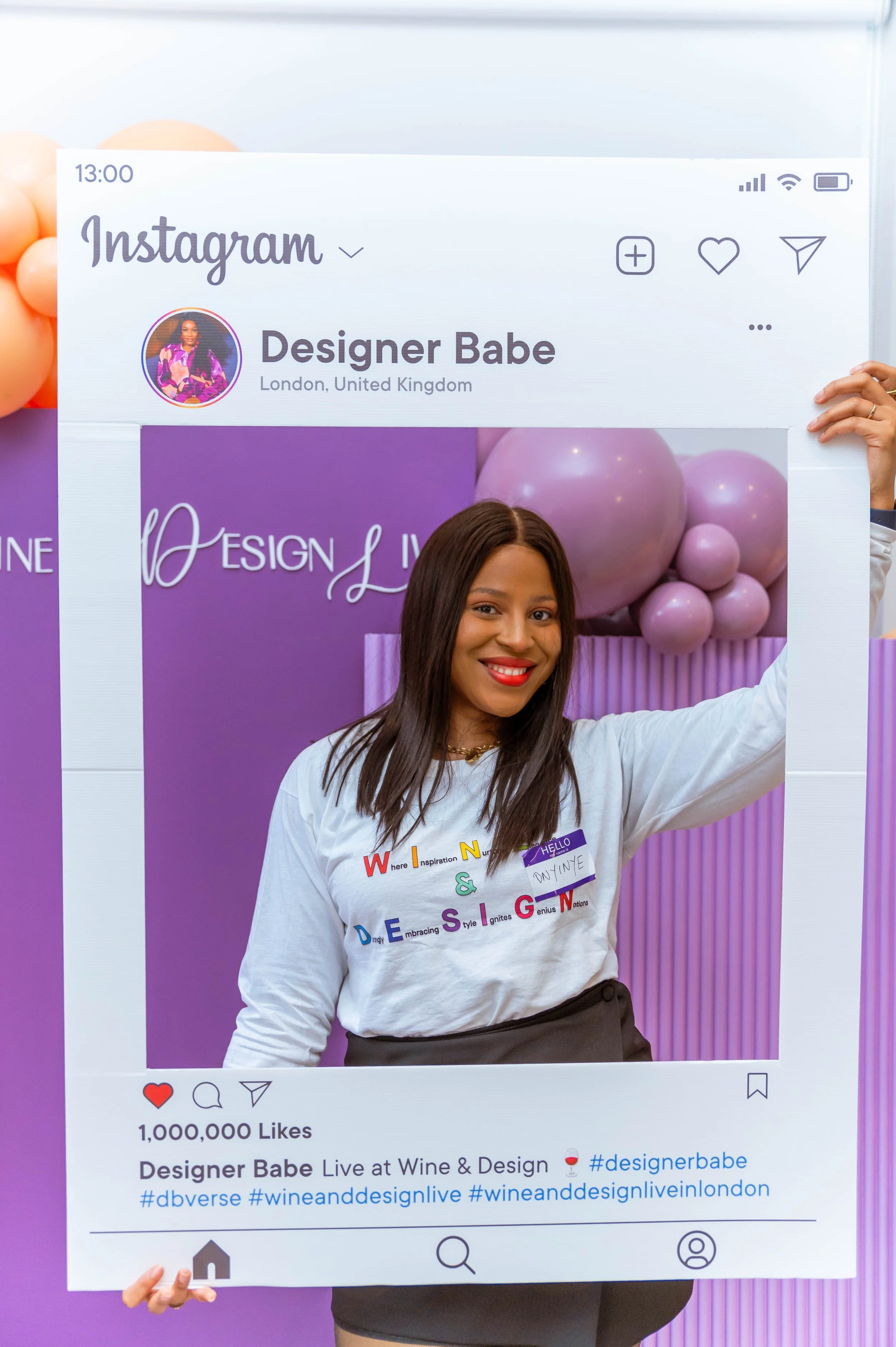 A woman holding a large Instagram photo frame at a wine and design event in London, smiling, with purple balloons in the background.