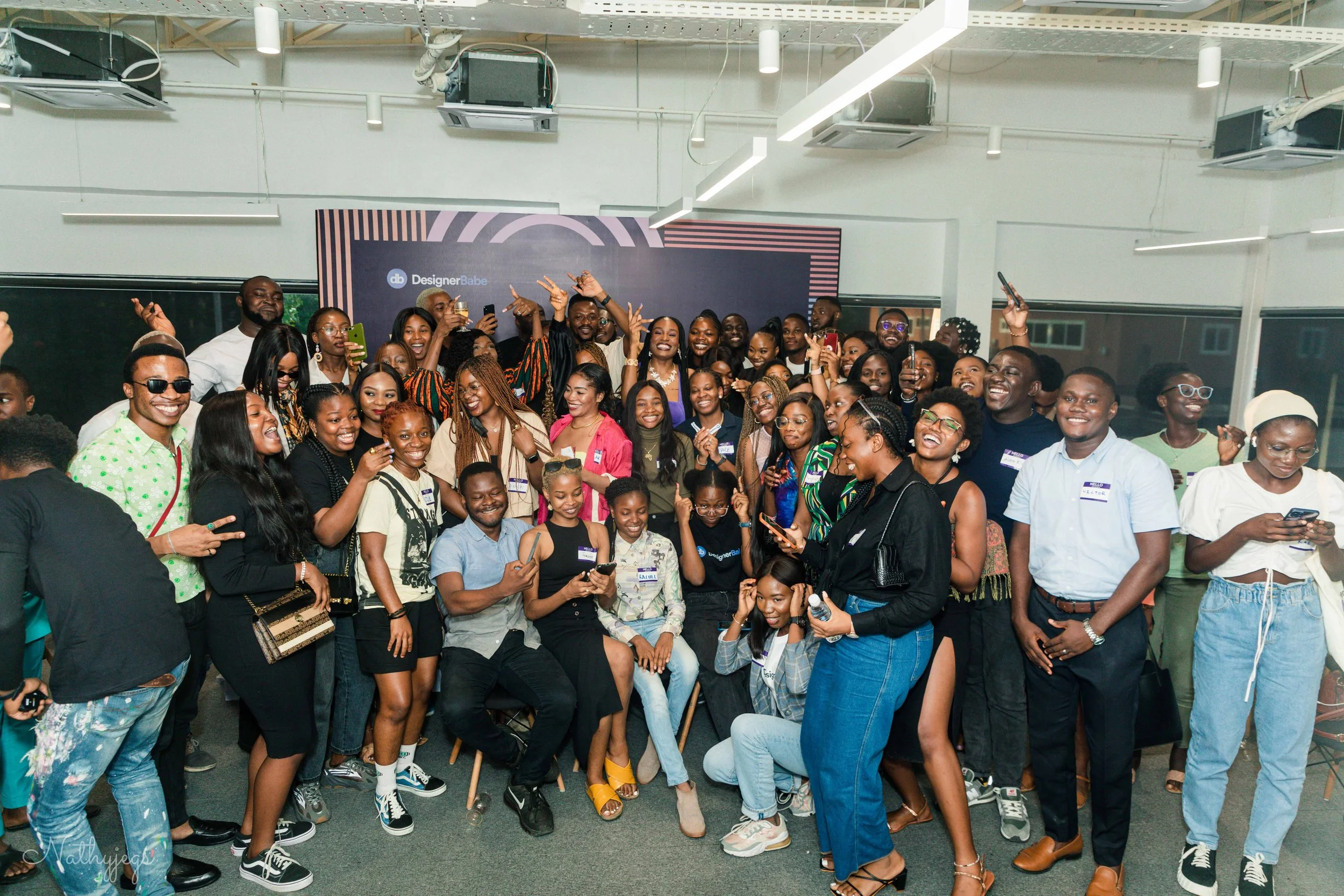 A large group of diverse people gathered in a conference or event room, smiling and posing for a picture, with some holding phones and others wearing name tags.