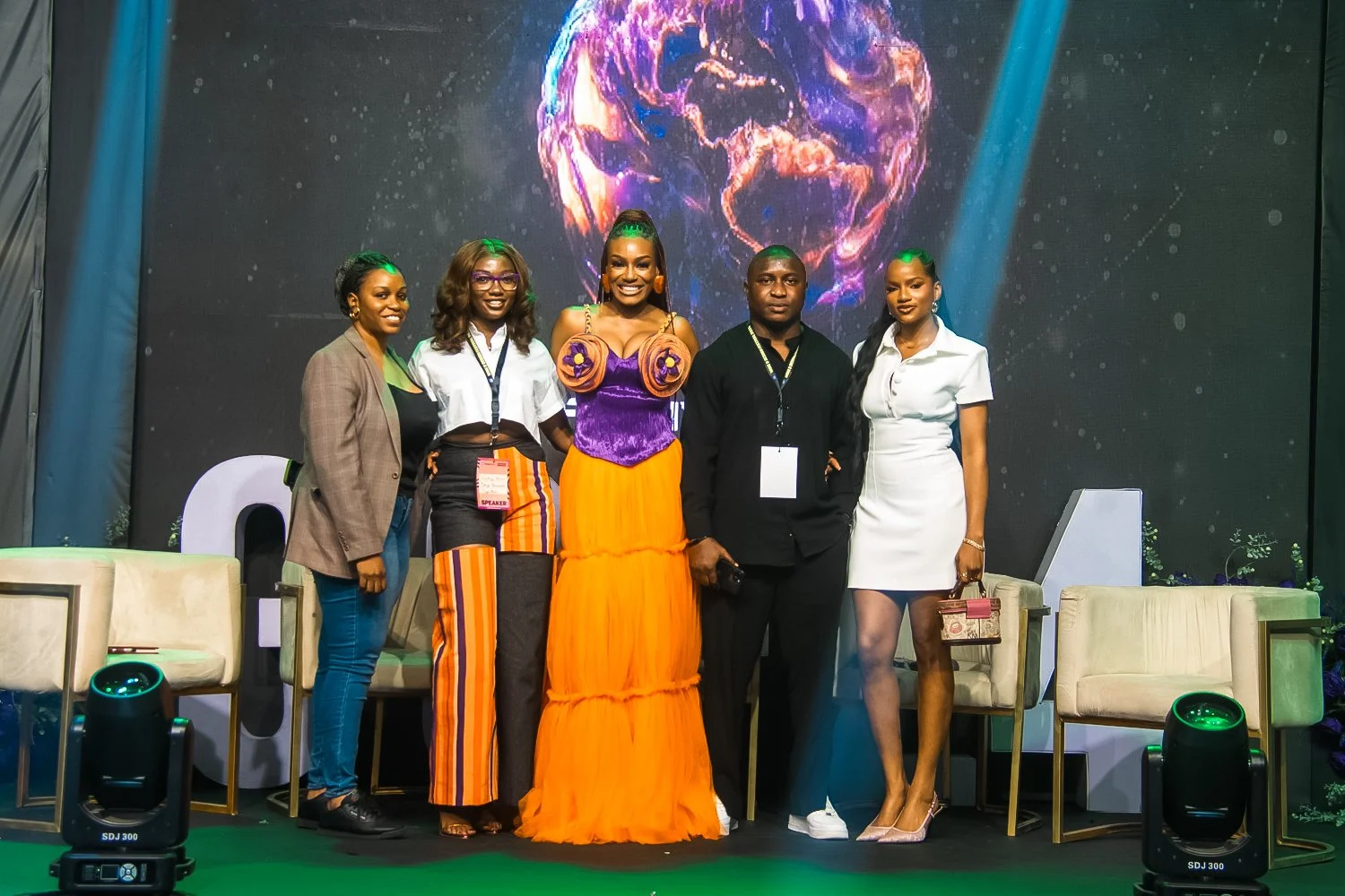 Group of five people standing on stage at a conference or event, with a backdrop featuring a colorful, swirling globe design.
